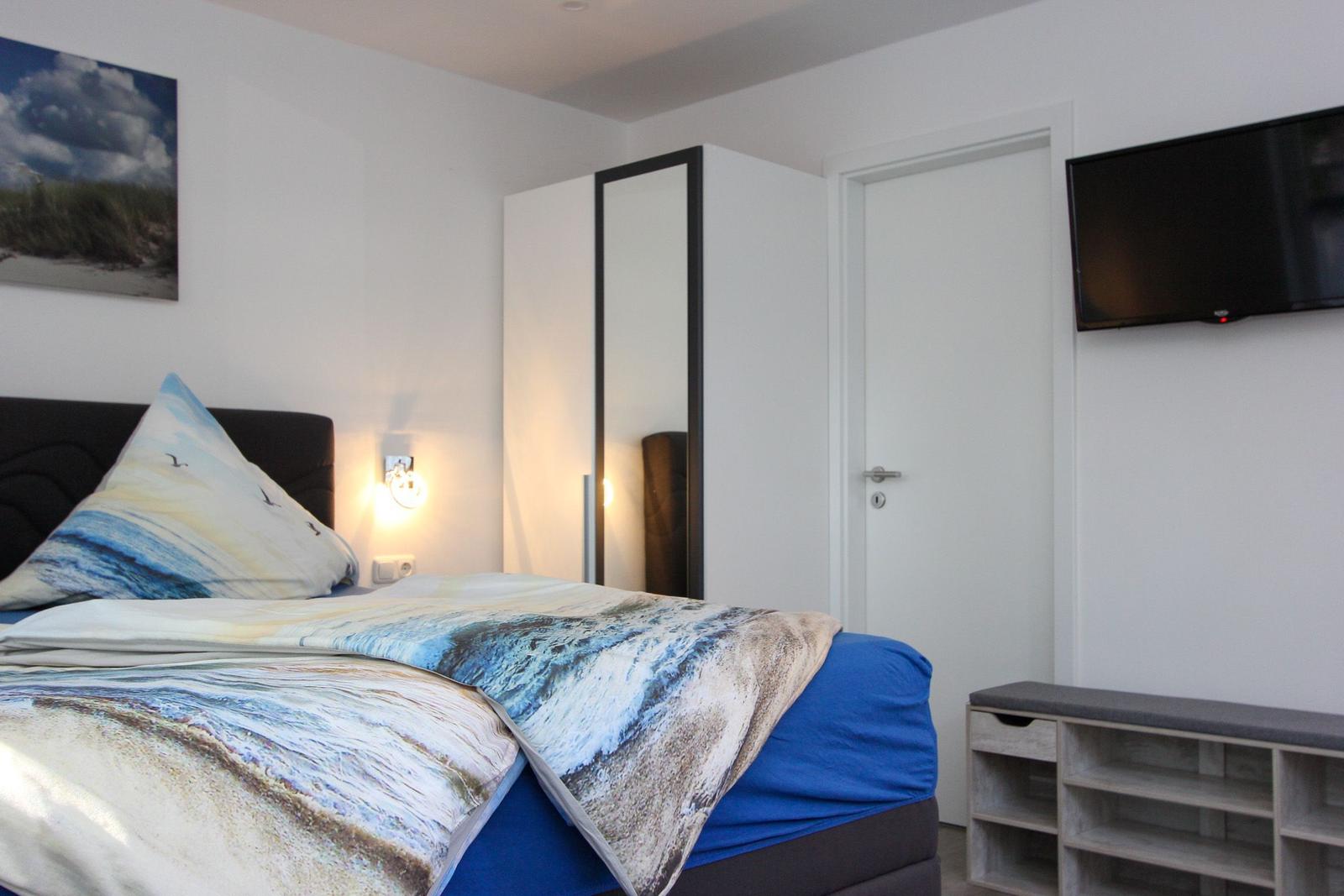 Schlafzimmer mit Bett, Wandbild, Spiegelschrank und Flachbildfernseher.