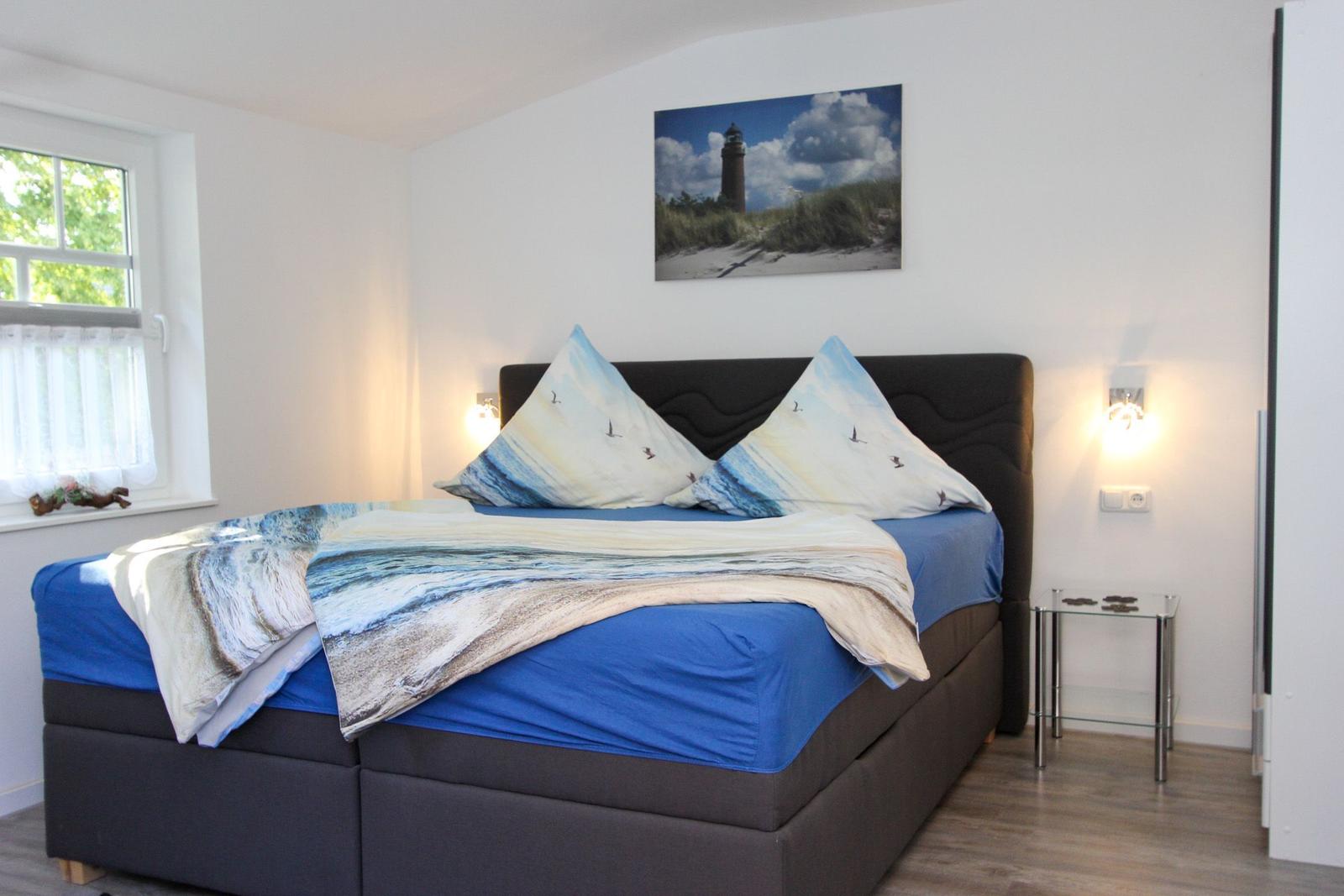 Schlafzimmer mit Bett, Wandbild und Nachttisch. Fenster mit Vorhängen.