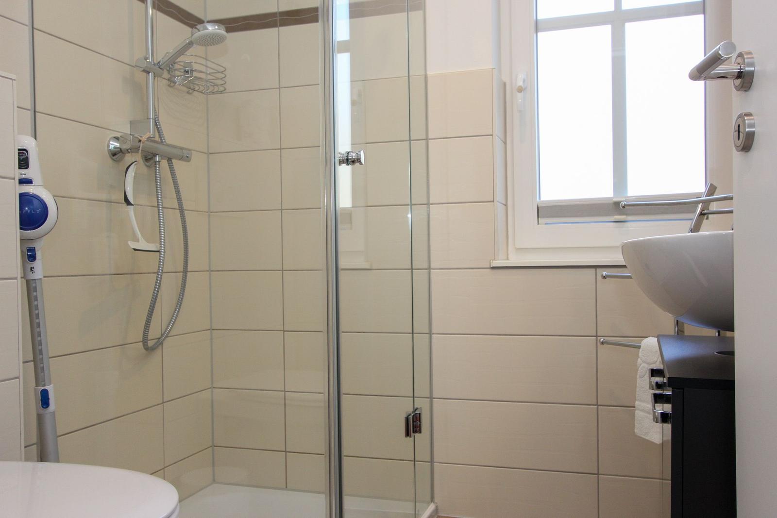 Badezimmer mit Dusche, Waschbecken und Fenster.