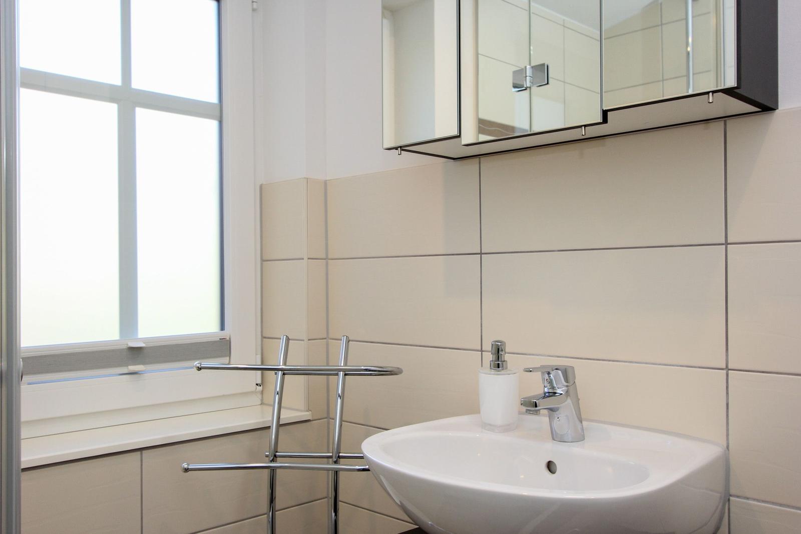 Badezimmer mit Waschbecken, Spiegelschrank und Fenster.