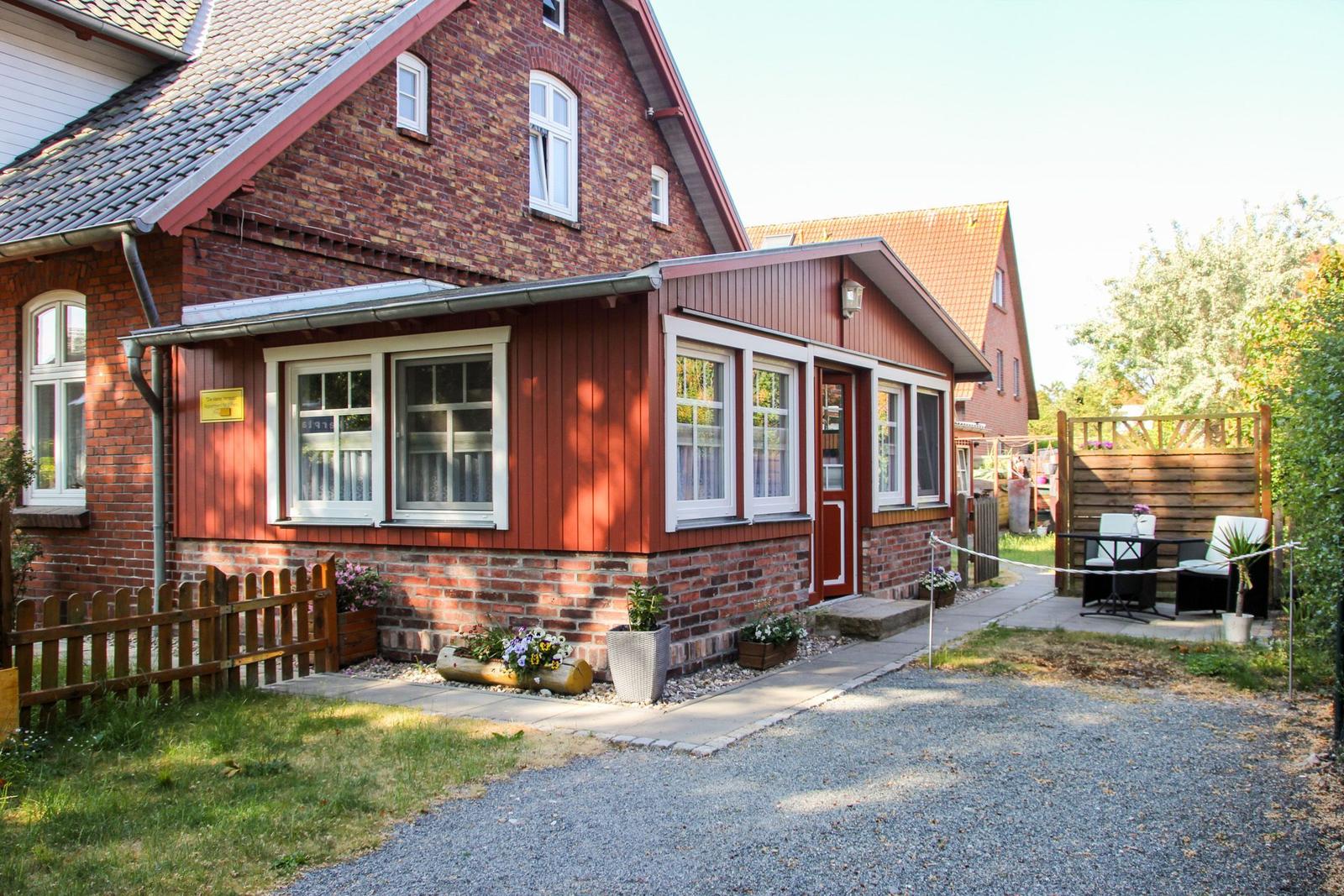 Rotes Holzhaus mit Garten und Terrasse. Eingangstür und Fenster mit weißen Rahmen.