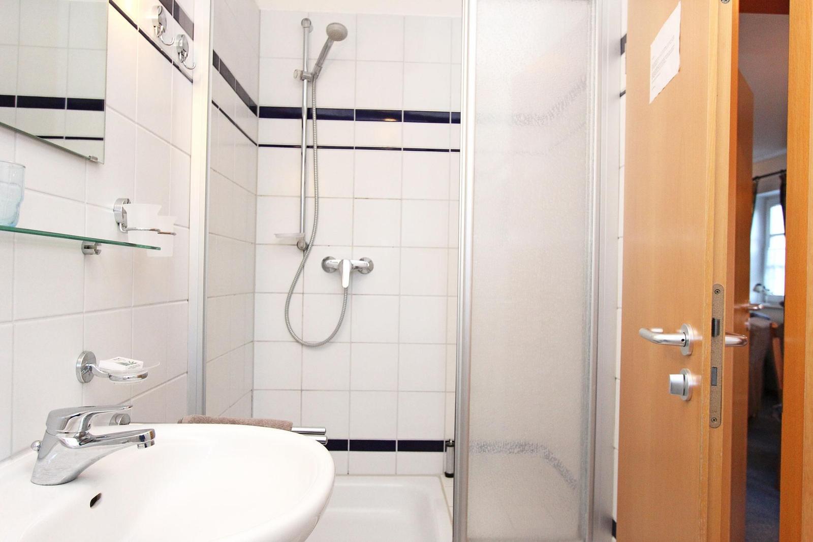 Badezimmer mit Dusche, Waschbecken und Spiegel. Tür führt in das Zimmer.