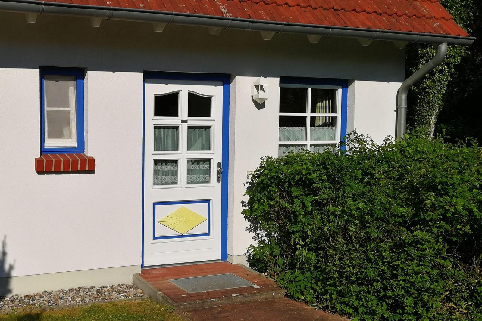 Eingangstür mit gelbem Sonnenmotiv, weiße Wände, blaue Fensterrahmen und roter Ziegeldach