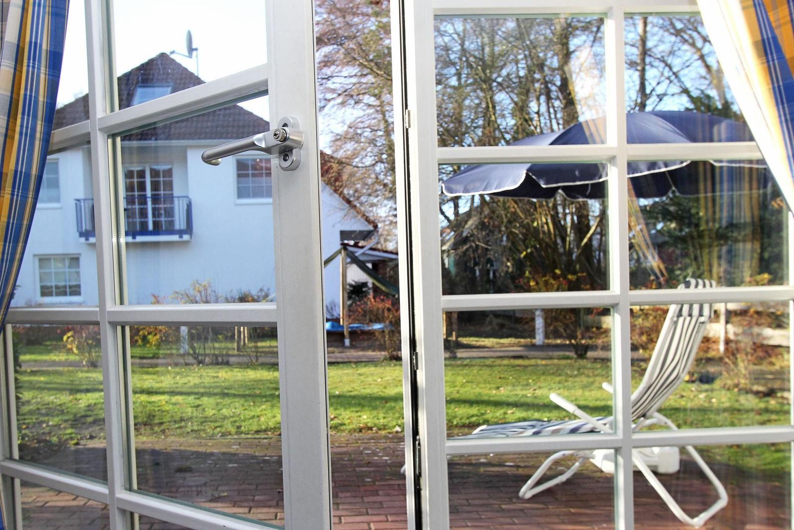 Durch die Glastüren ist ein Garten mit Liegestuhl und Sonnenschirm zu sehen.