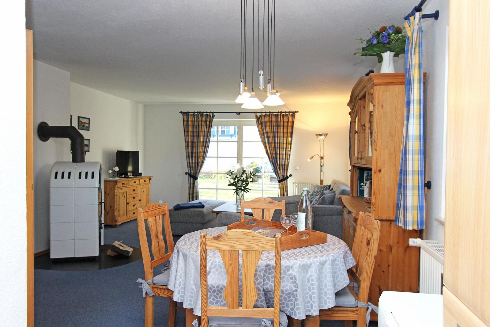 Esszimmer mit Holztisch und Stühlen. Wohnbereich mit Sofa und Kaminofen.