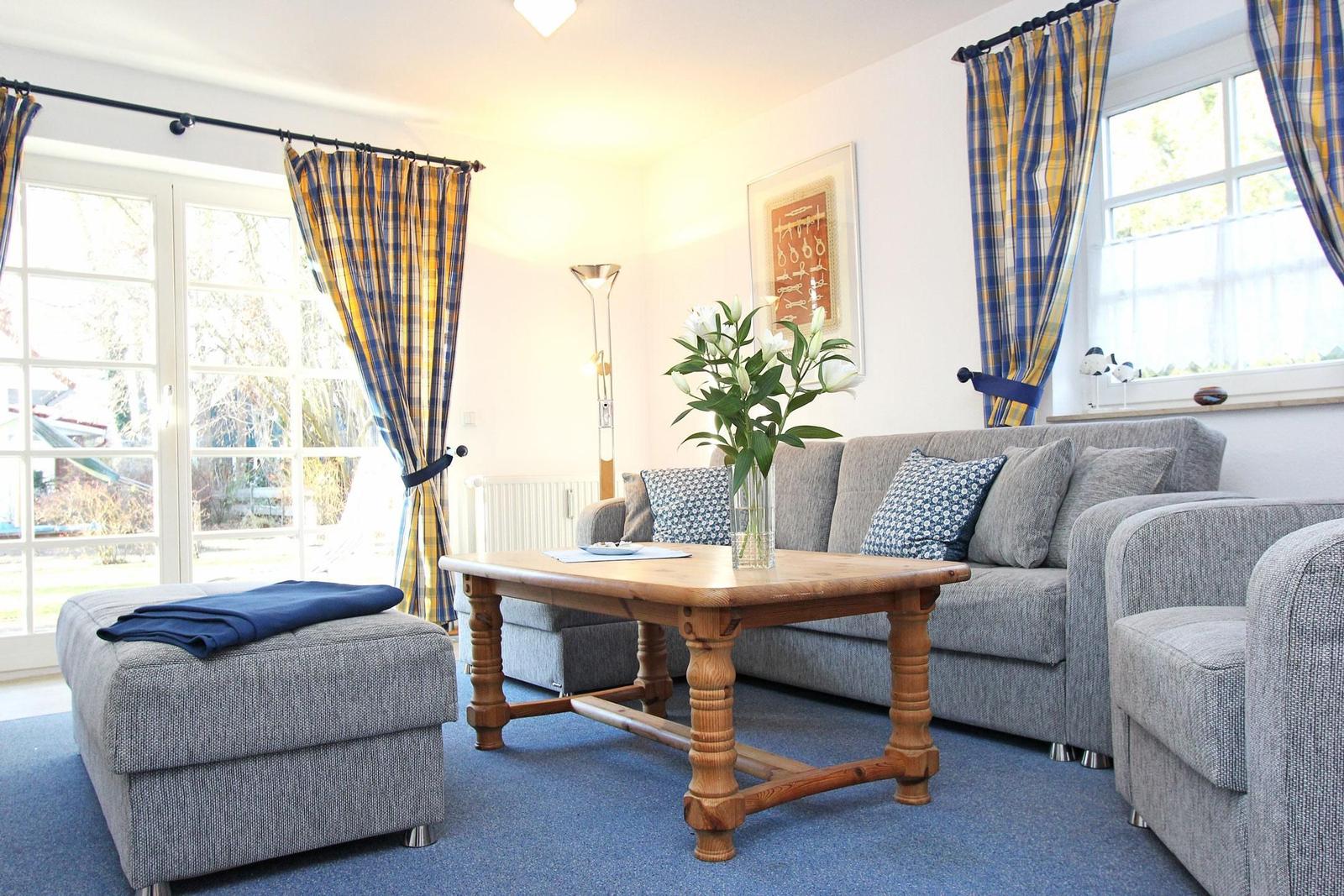 Wohnzimmer mit grauem Sofa, Holztisch und blauen Gardinen.