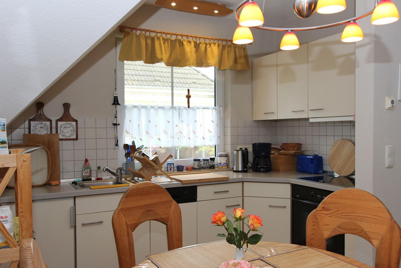 Küche mit Essbereich, Holzmöbeln und Fenster mit Vorhängen.