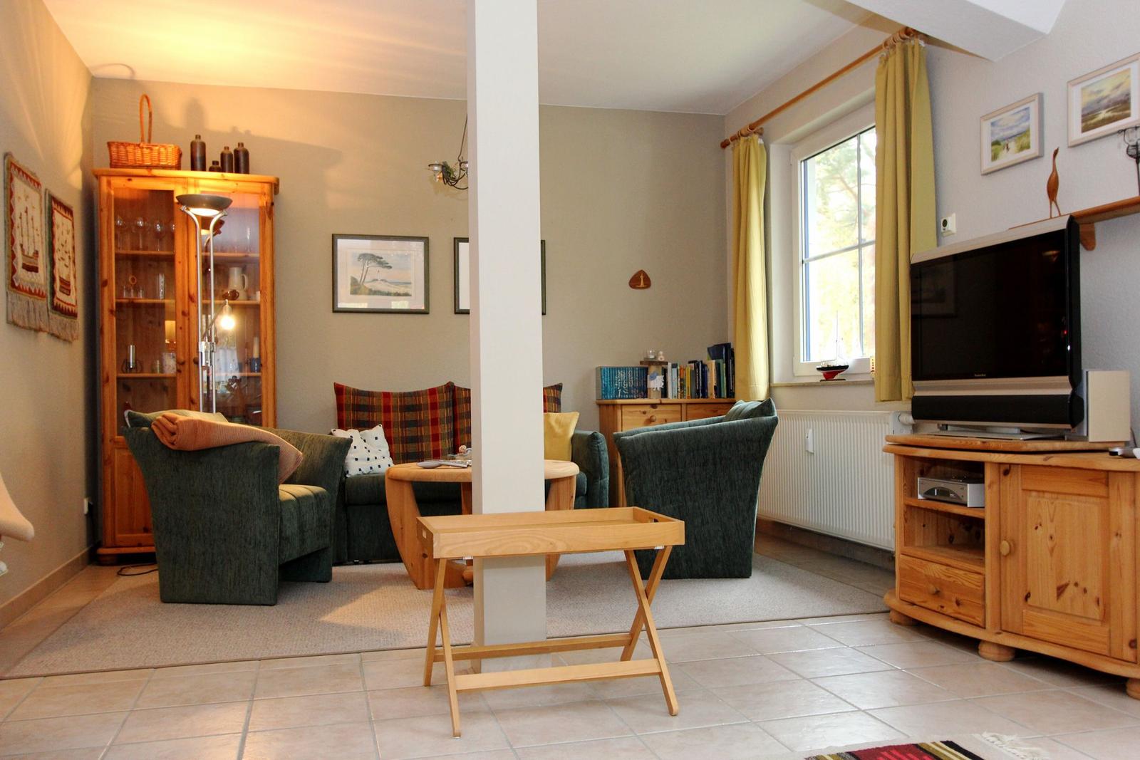 Wohnzimmer mit Sofa, Fernseher und Holzmöbeln. Fenster mit gelben Vorhängen.