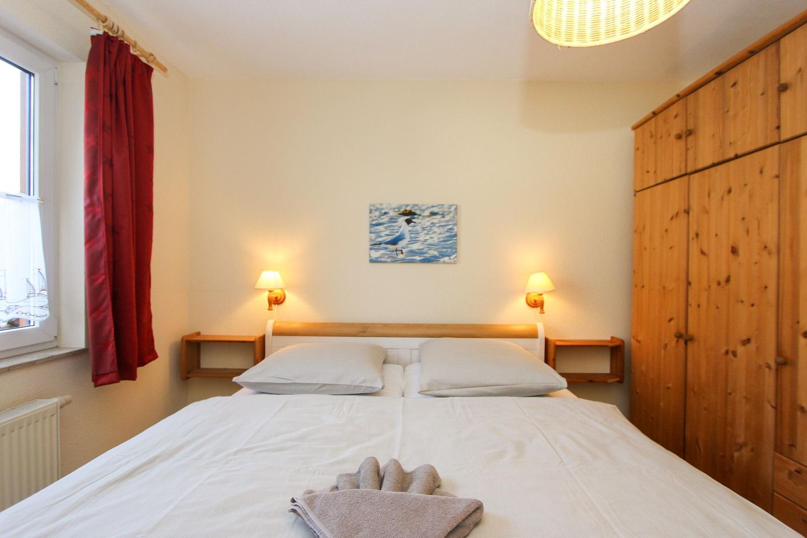 Schlafzimmer mit Doppelbett, Holzschrank und Wandbild mit Vogel.