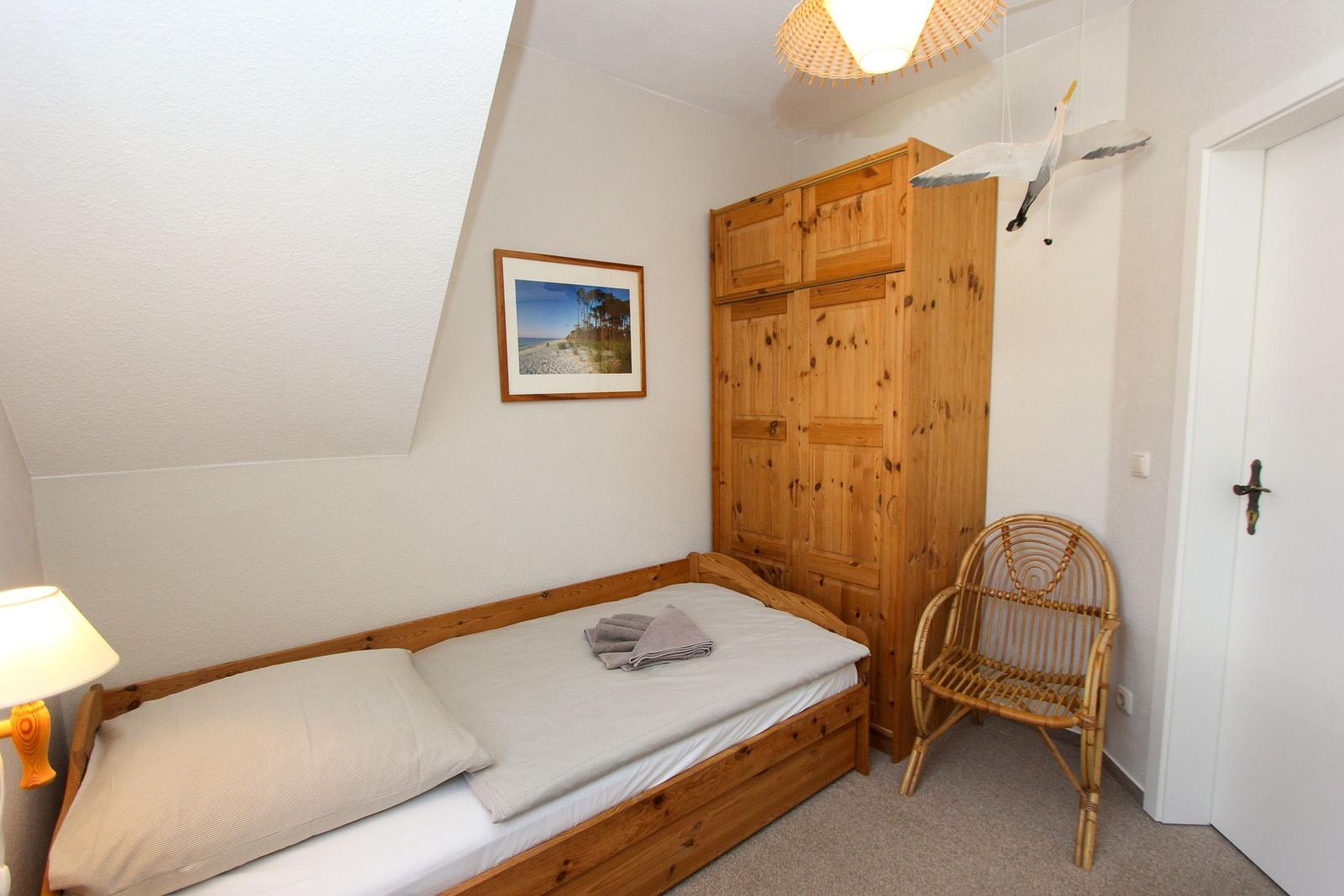 Ein Schlafzimmer mit Holzbett, Kleiderschrank und Stuhl. An der Wand hängt ein Bild.