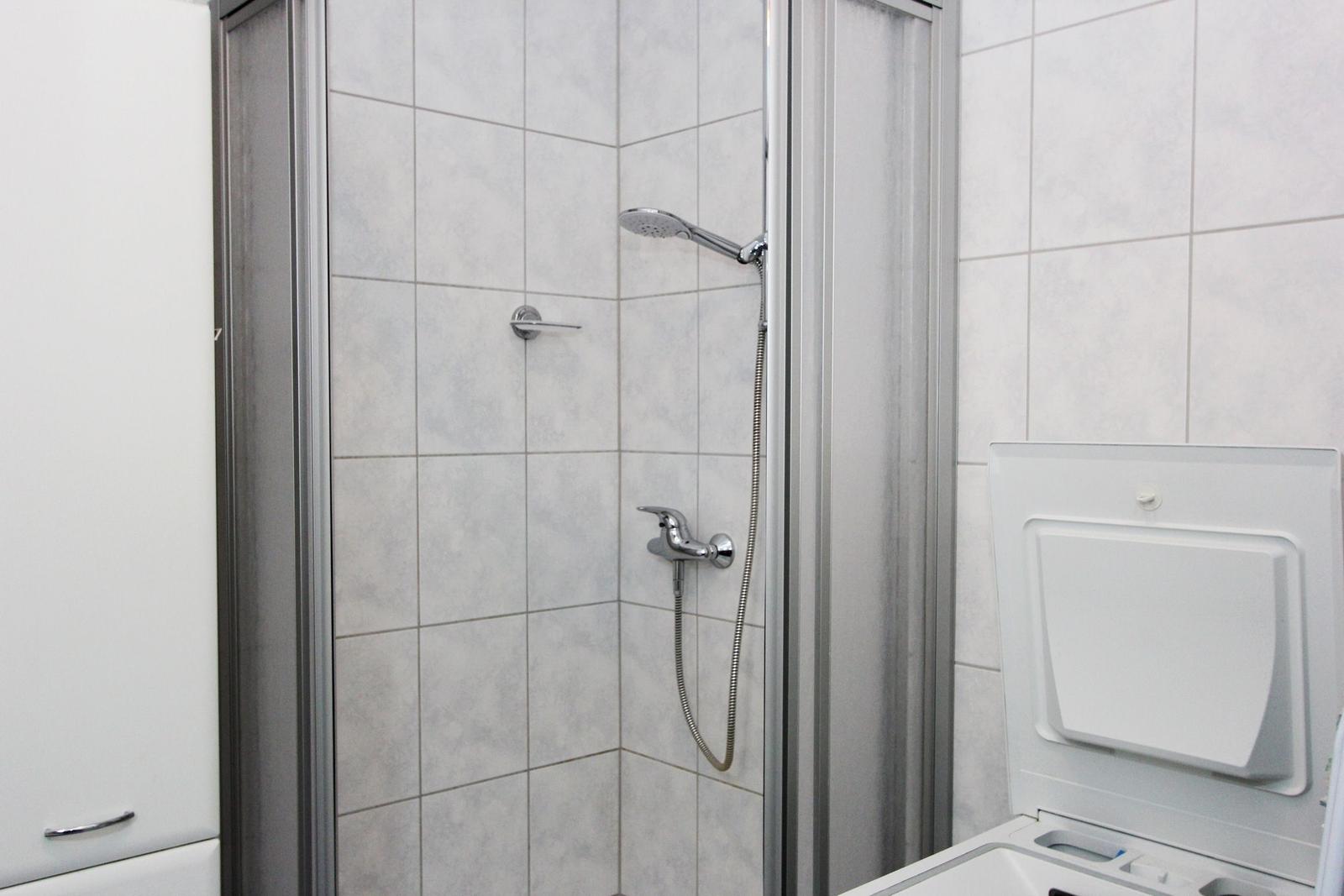 Dusche mit Handbrause und Waschmaschine in Badezimmer