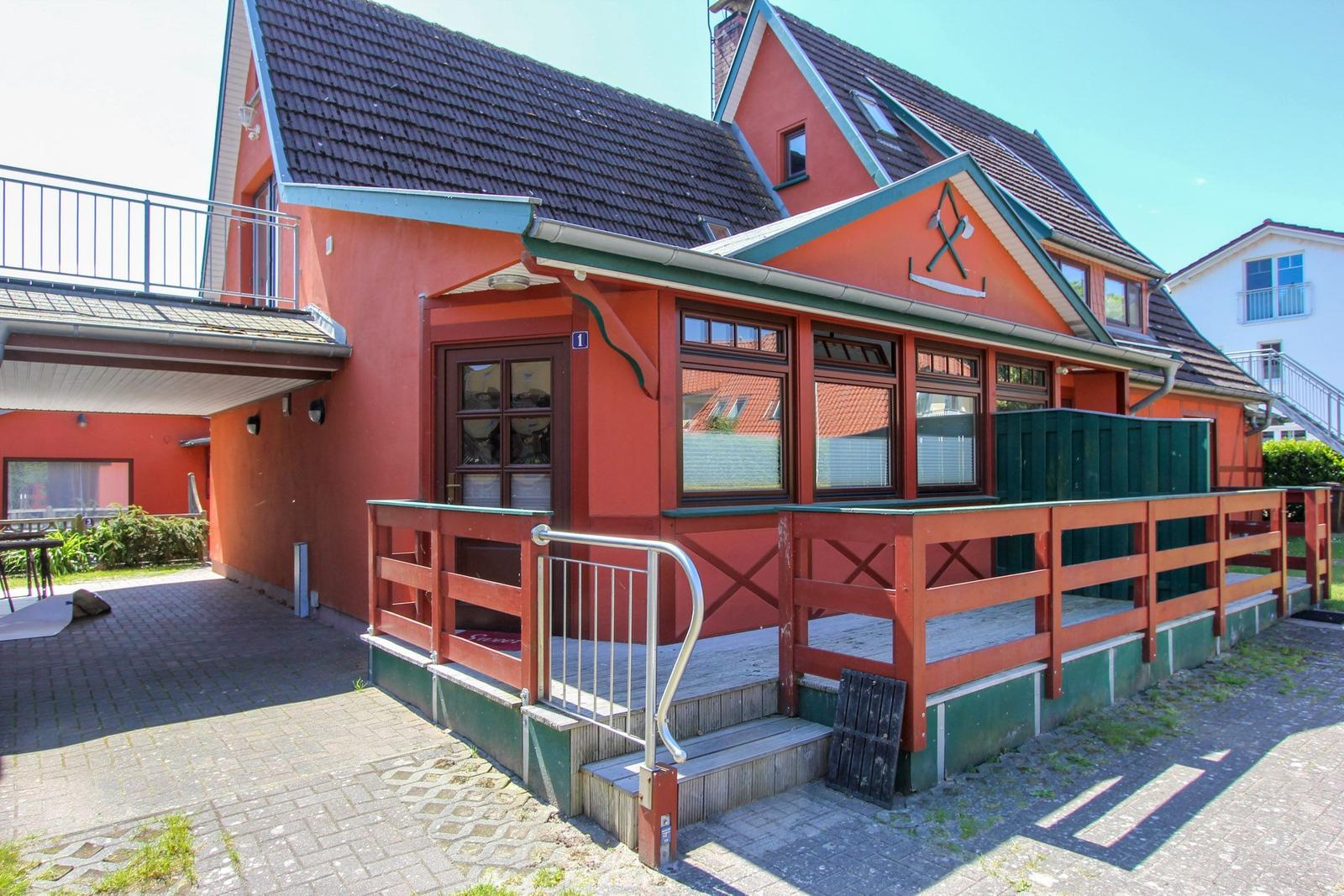 Rotes Ferienhaus mit Terrasse und Holzgeländer. Eingangstür und Fenster sind sichtbar.