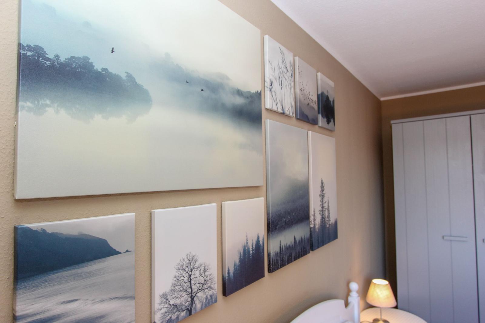 Wand mit mehreren Landschaftsbildern in Blau- und Grautönen, daneben Schrank und Nachttischlampe.