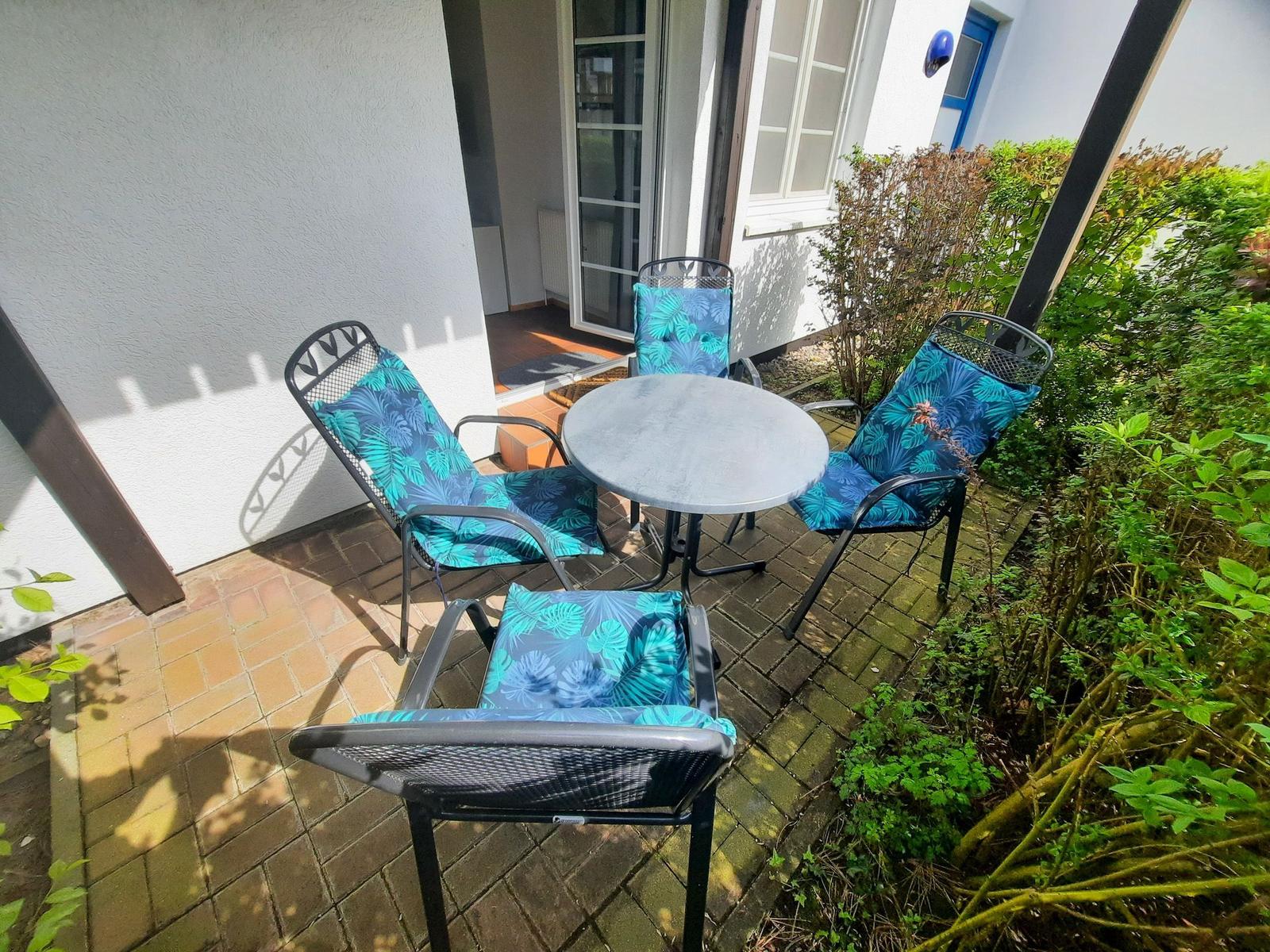 Terrasse mit runder Tisch und vier Stühlen mit blau-tropischen Kissen.