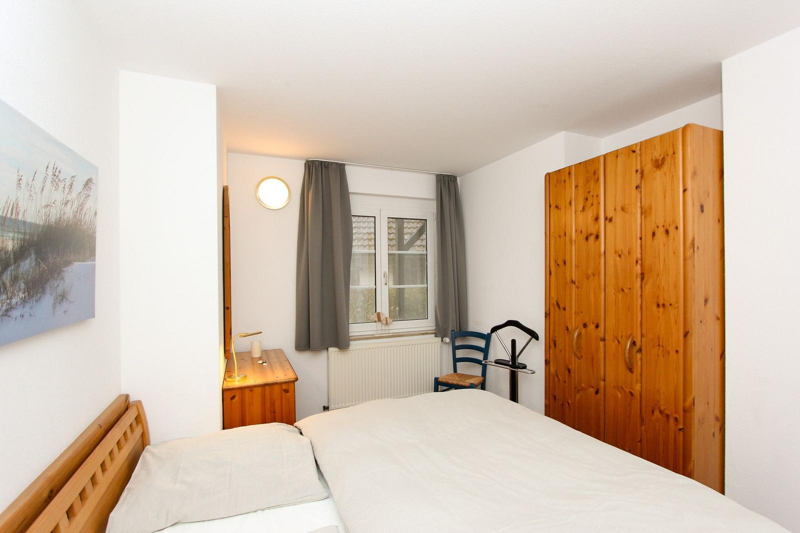 Schlafzimmer mit Bett, Holzschrank, Nachttisch und Fenster mit Vorhängen.