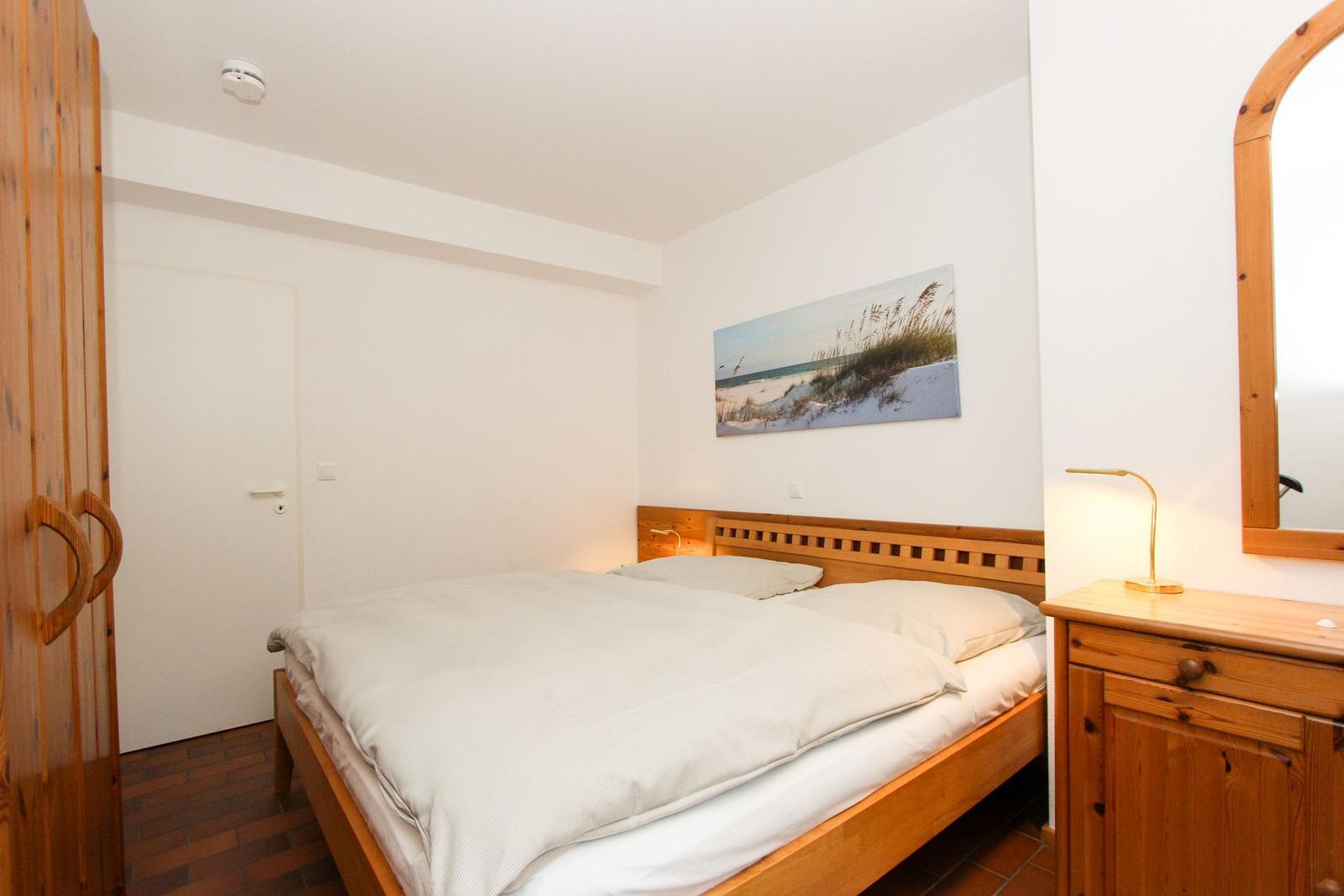 Schlafzimmer mit Holzbett, Kleiderschrank und Nachttisch mit Lampe.
