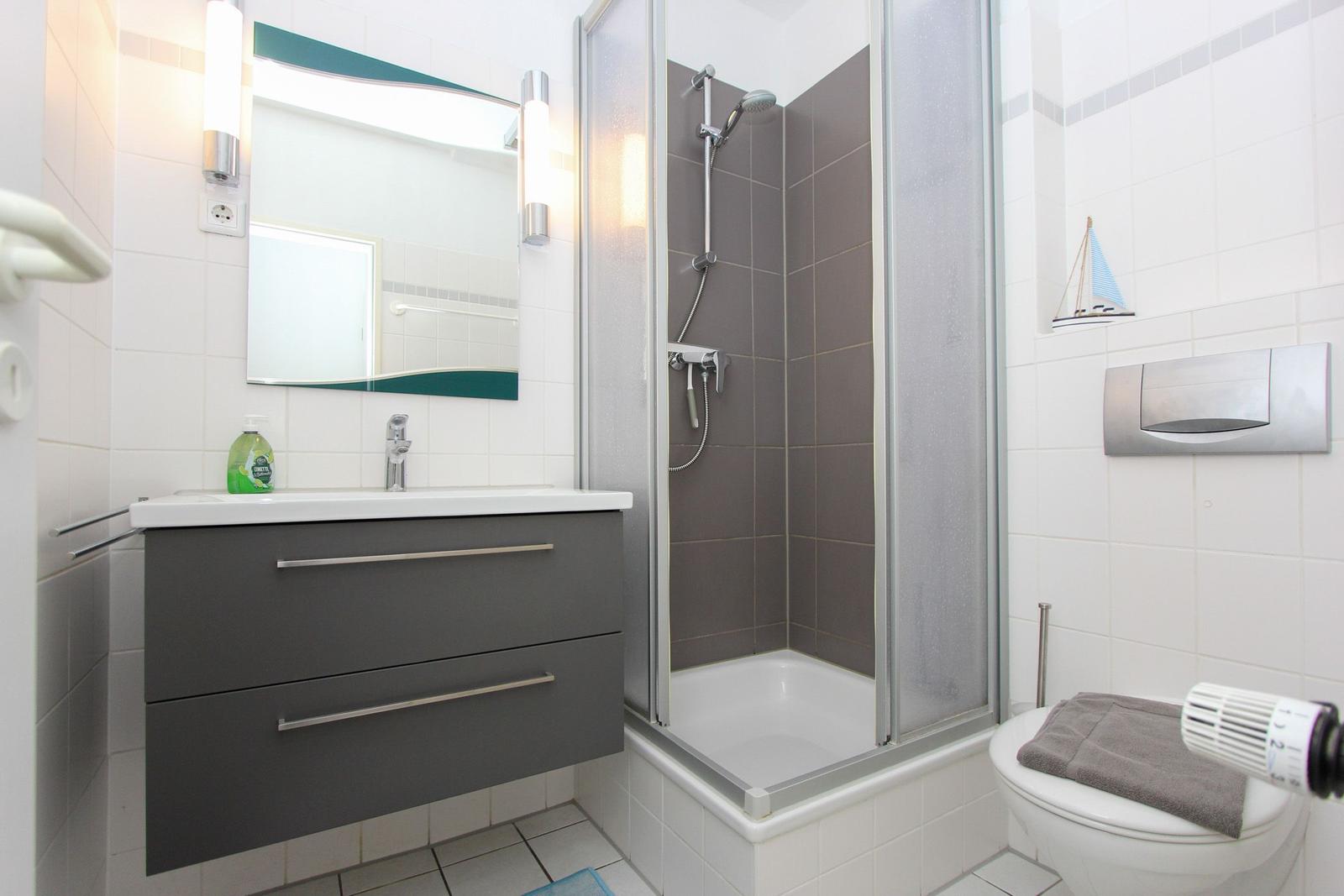 Badezimmer mit Dusche, Waschbecken und Toilette. Fliesenwand und Spiegel.