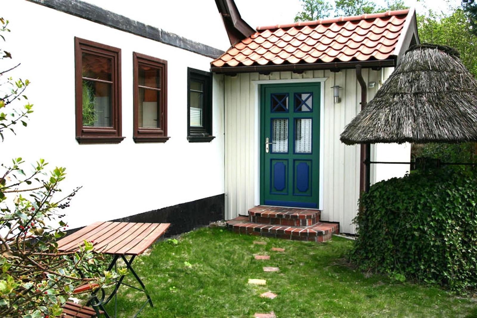 Haus mit grüner Tür, rotem Dach und Garten mit Tisch.