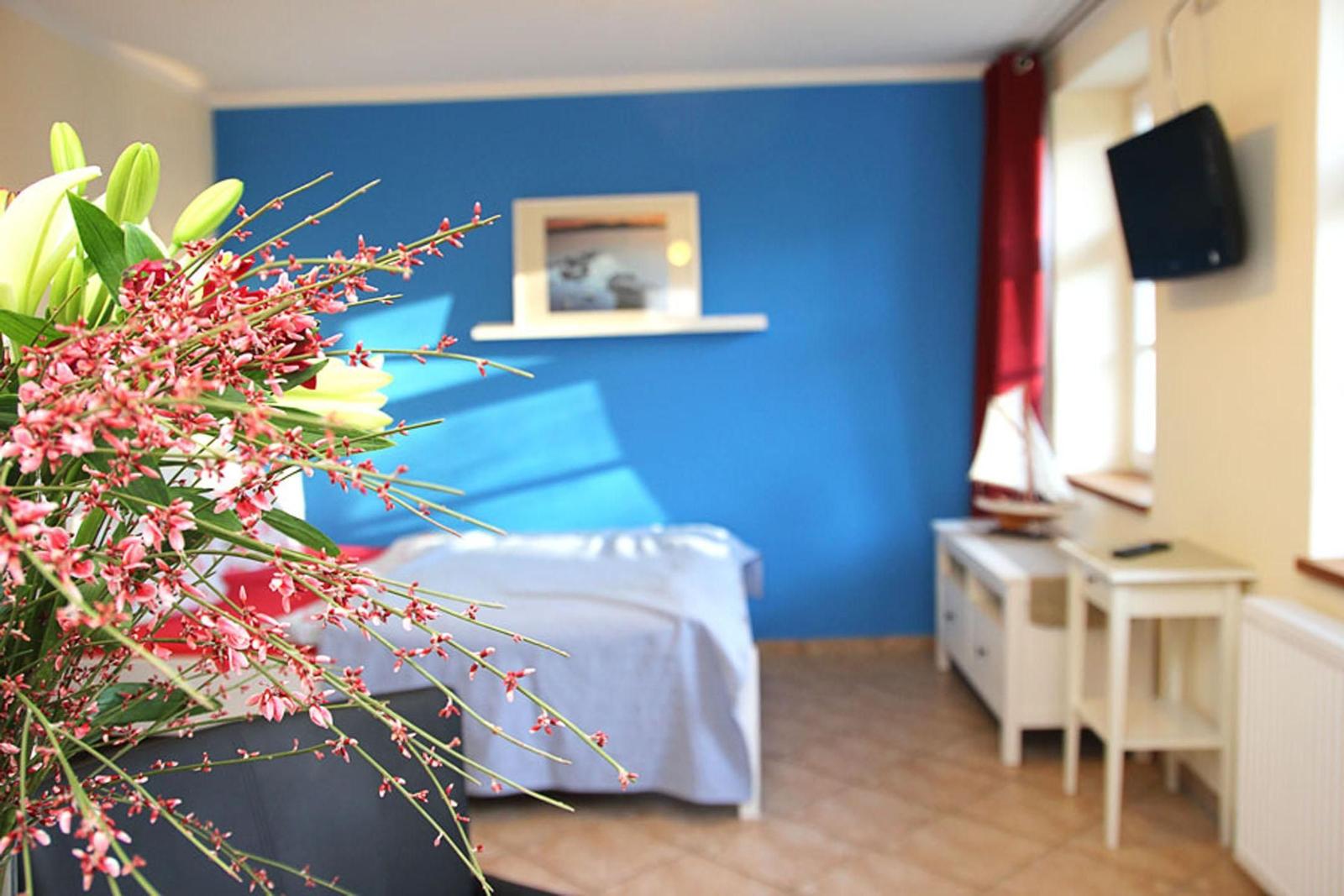 Schlafzimmer mit blauer Wand, Bett, Schreibtisch und Blumenarrangement.