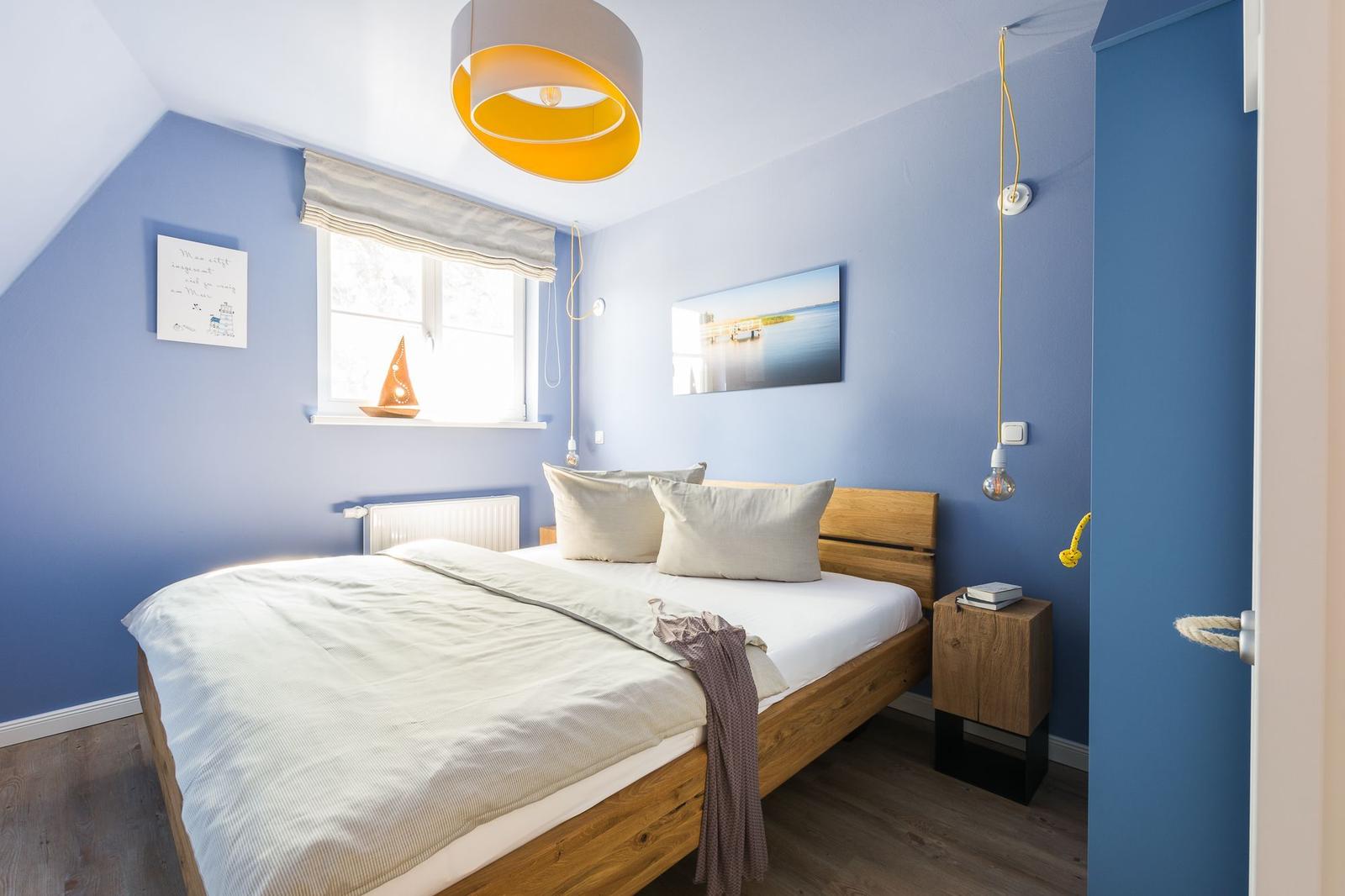 Schlafzimmer mit blauen Wänden, Holzbett und Fenster mit Segelboot.