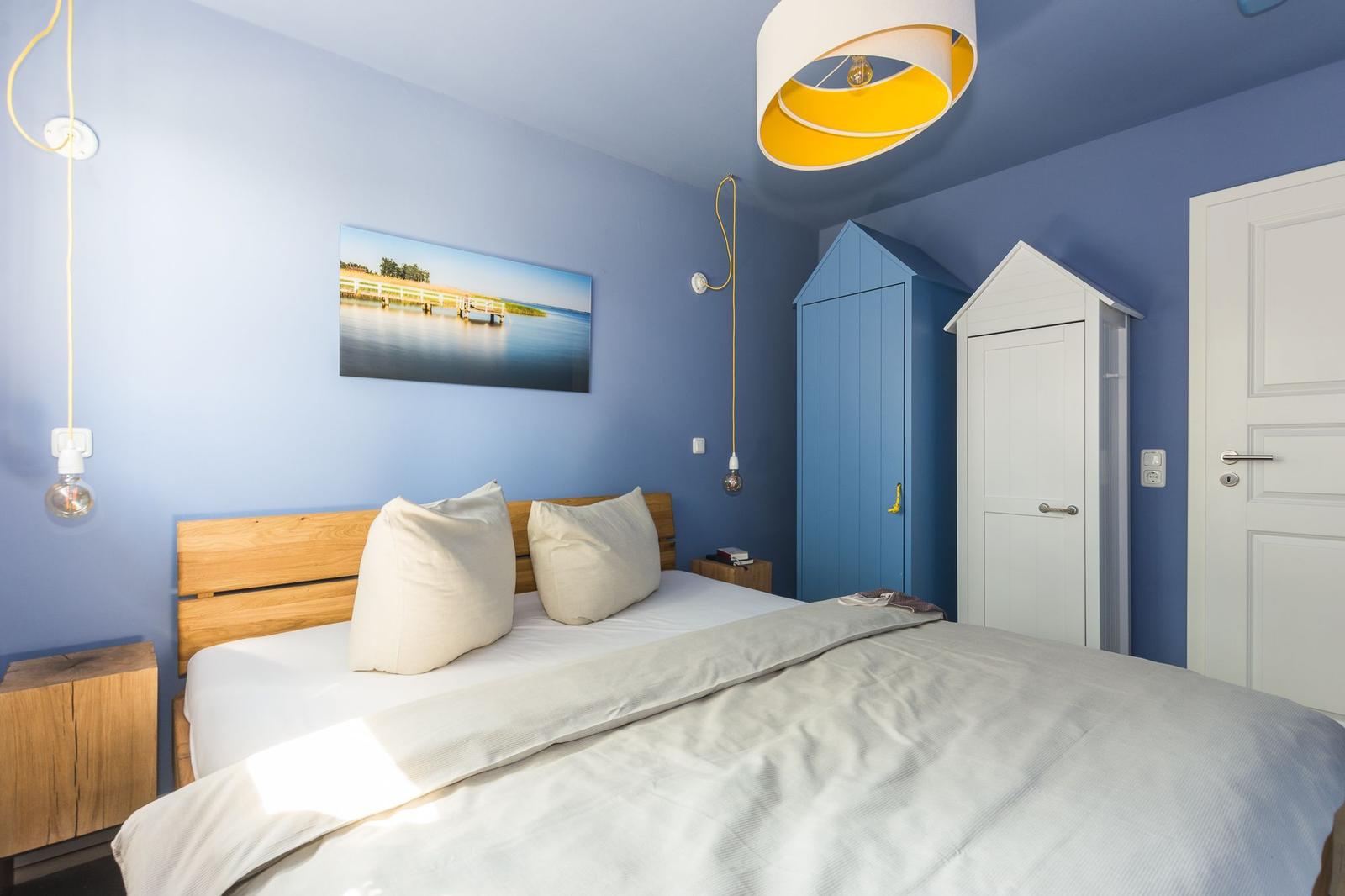 Schlafzimmer mit blauen Wänden, Bett, zwei Kleiderschränke und Wandbild.