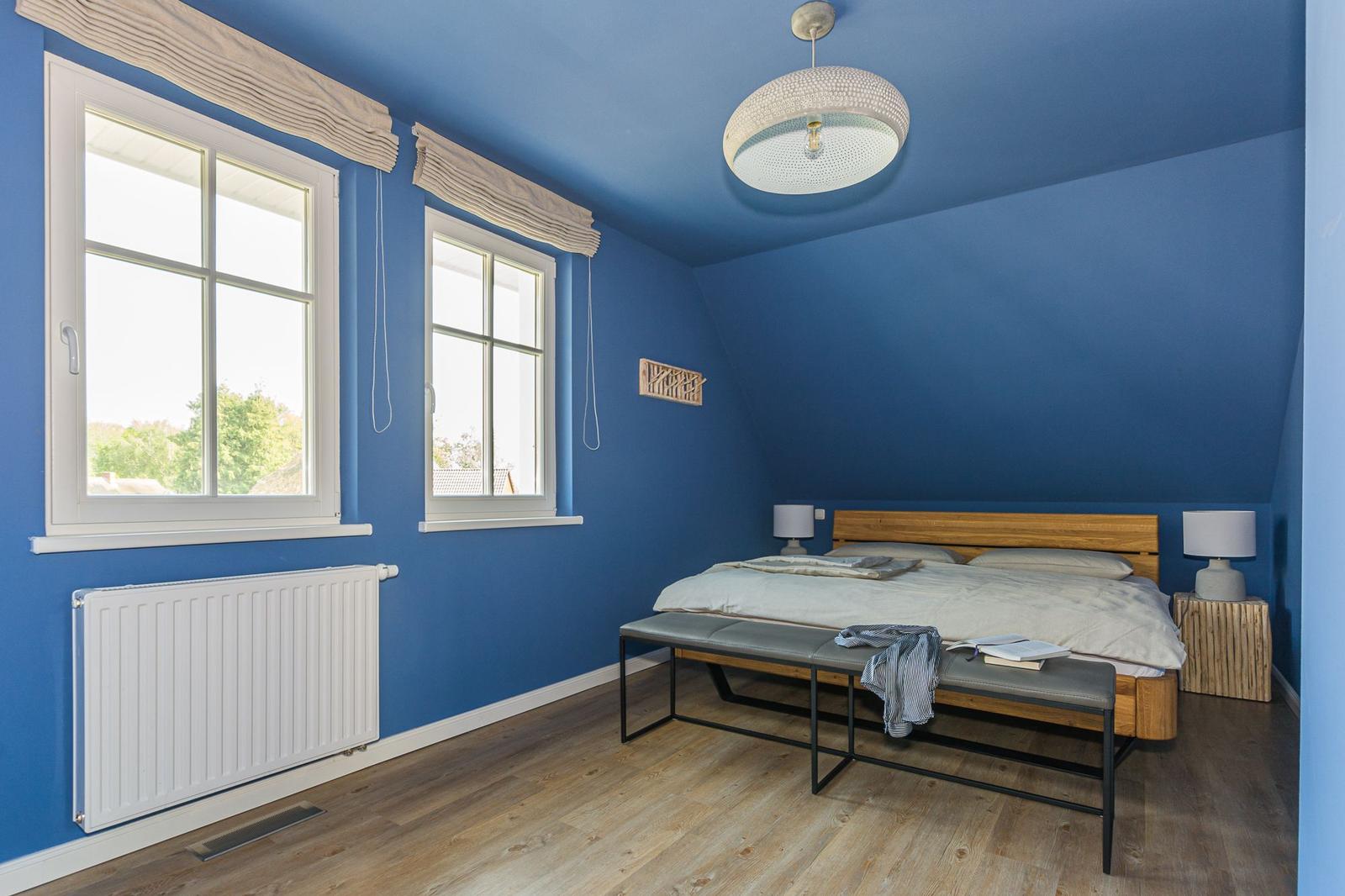 Schlafzimmer mit blauen Wänden, Holzboden und Bett mit Holzkopfteil.