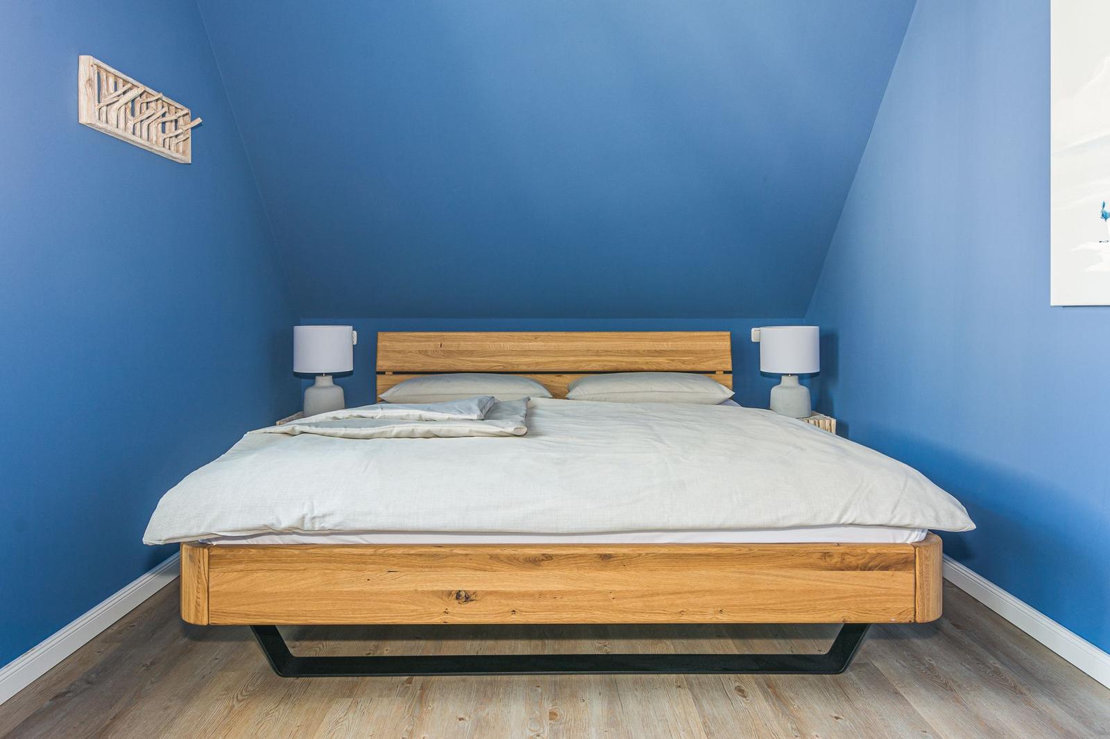 Schlafzimmer mit Holzbett, blauen Wänden und zwei Nachttischen mit Lampen.