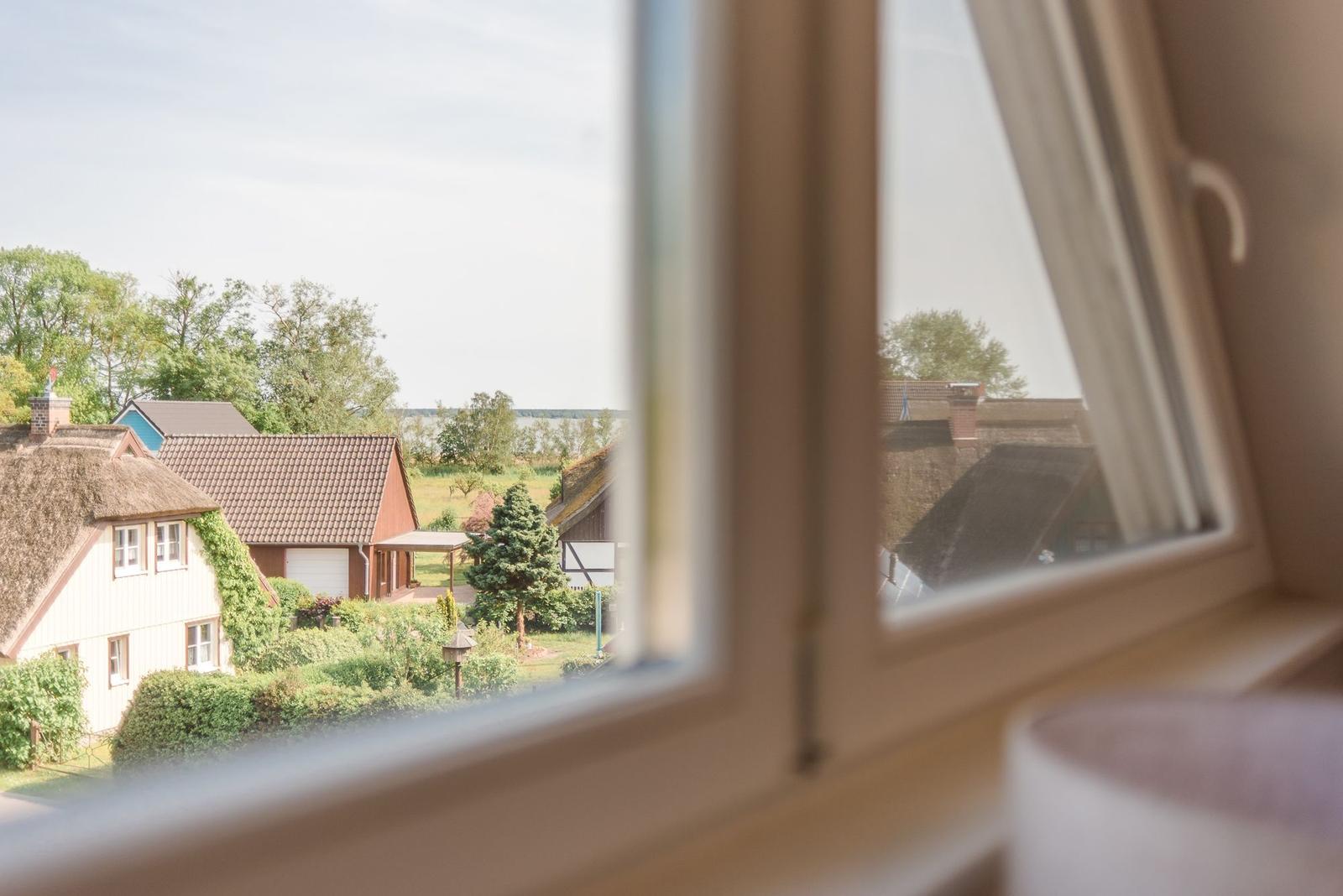 Durch das Fenster blickt man auf ein Dorf mit Strohdächern und Grünflächen.