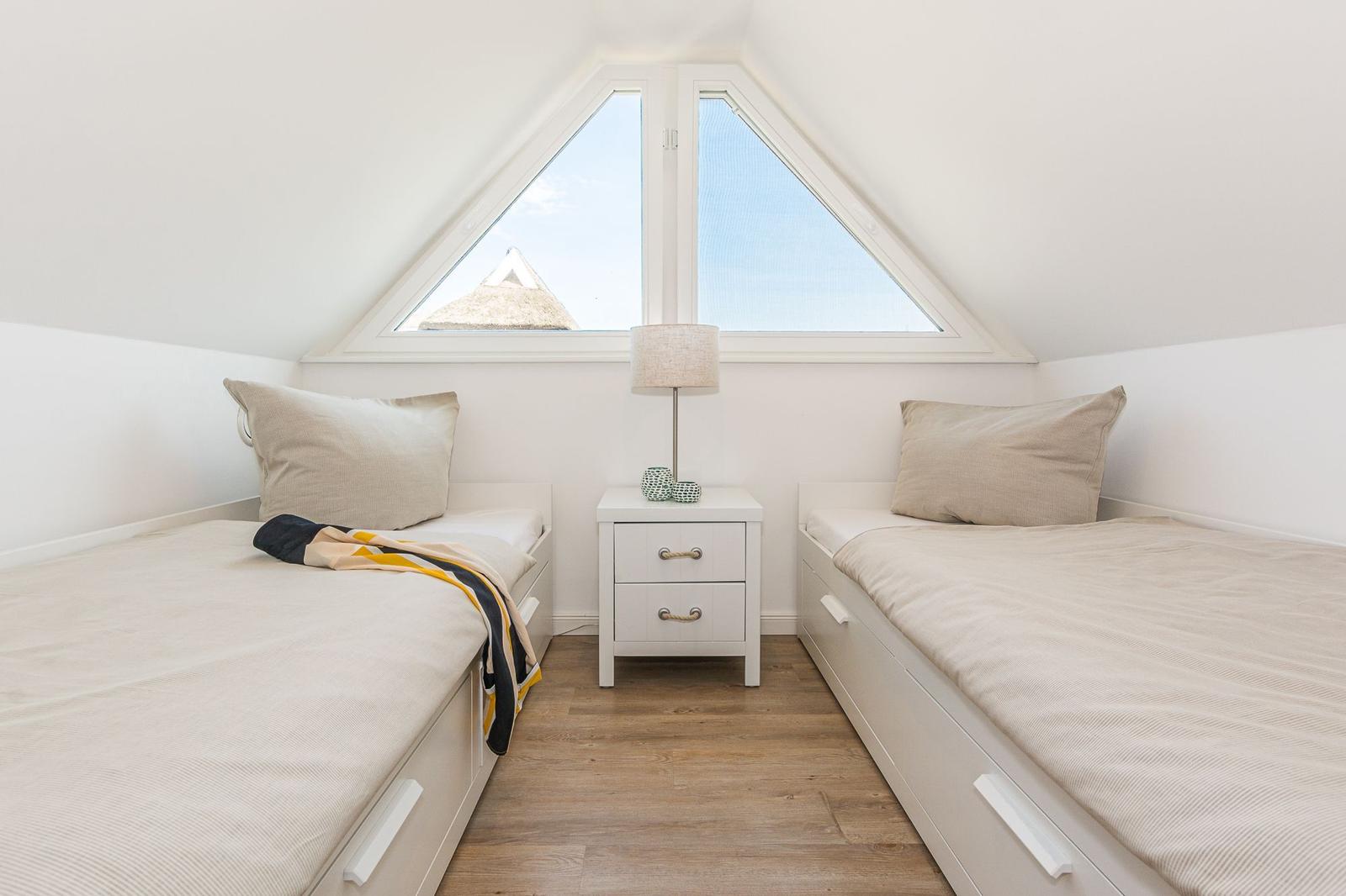 Zwei Schlafstellen mit Matratzen und Kissen unter einem Dachfenster mit Blick auf eine Hütte.