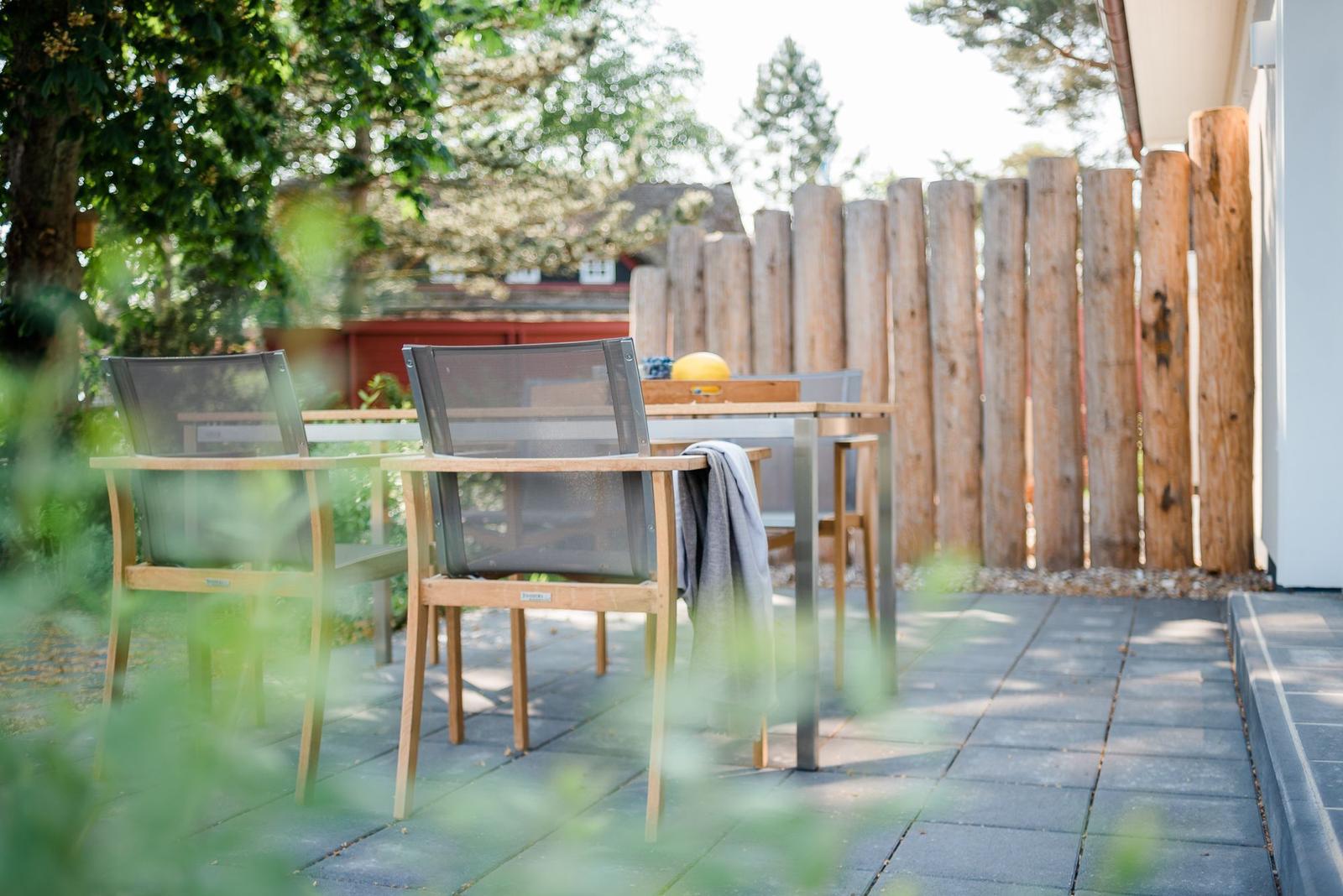 Terrasse mit Tisch und Stühlen, Holzgeländer und Bäumen im Hintergrund.