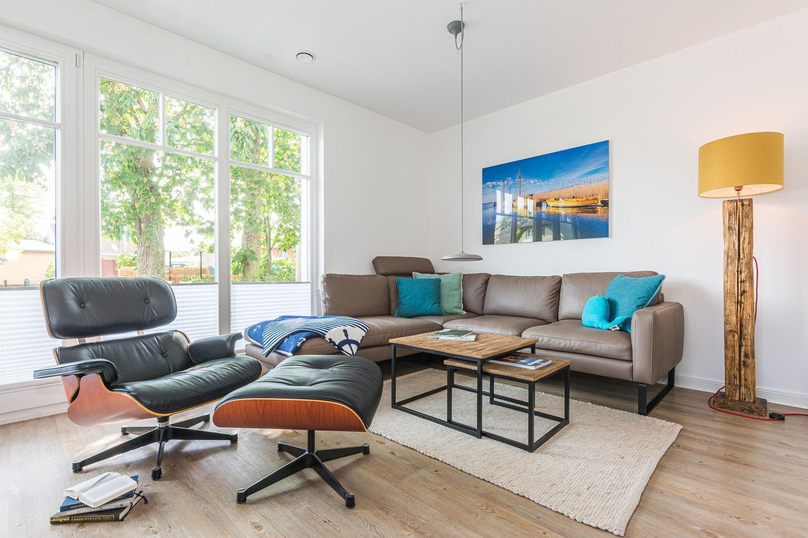 Wohnzimmer mit braunem Sofa, Ecksessel und Holzboden. Große Fenster und Wandbild.