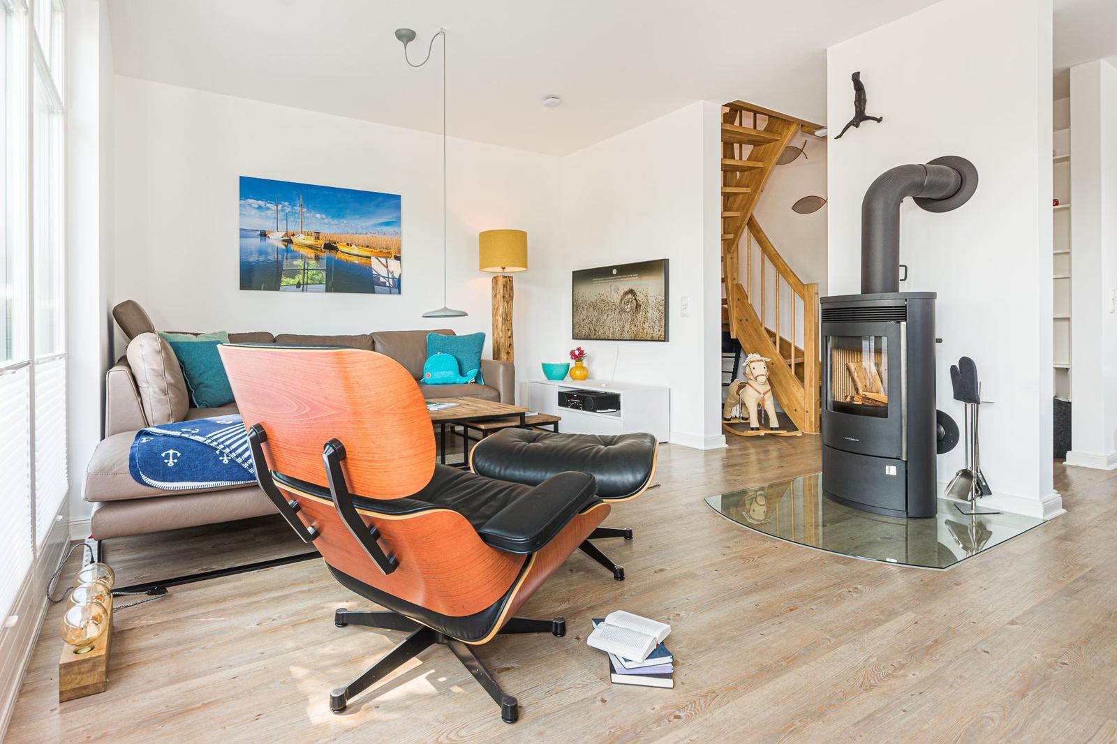 Wohnzimmer mit Holzboden, Sofa, Stuhl und Kaminofen. Treppenhaus und Wandbild sind sichtbar.
