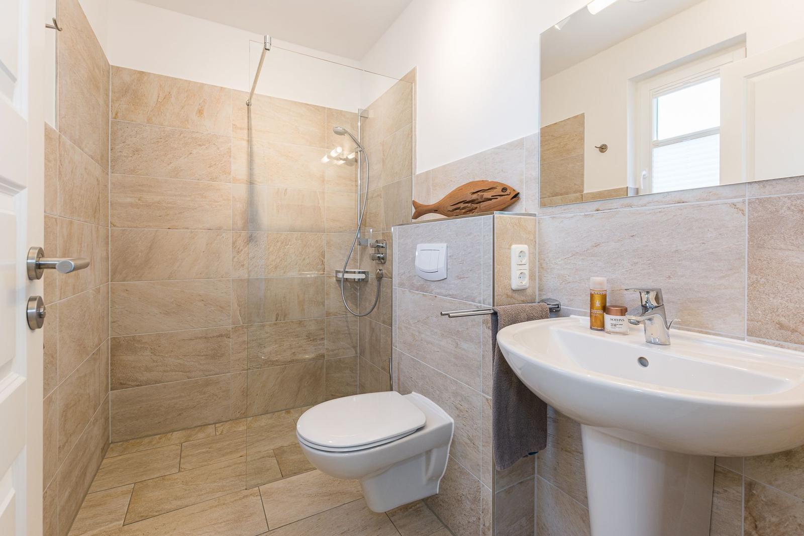 Badezimmer mit Dusche, Toilette und Waschbecken. Wandfliesen und Spiegel sichtbar.