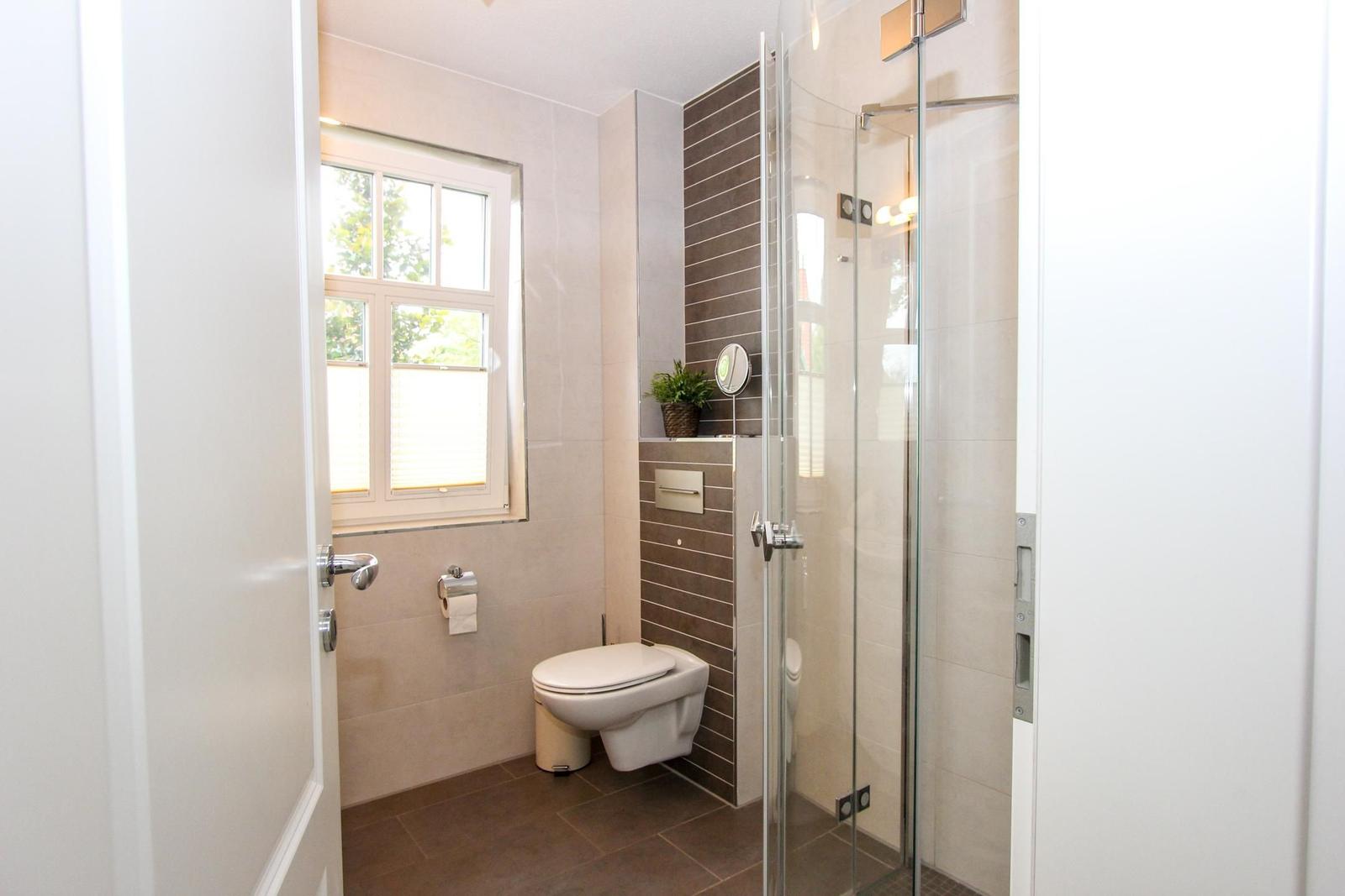Badezimmer mit Dusche, Toilette und Fenster. Fliesenwand und Boden.