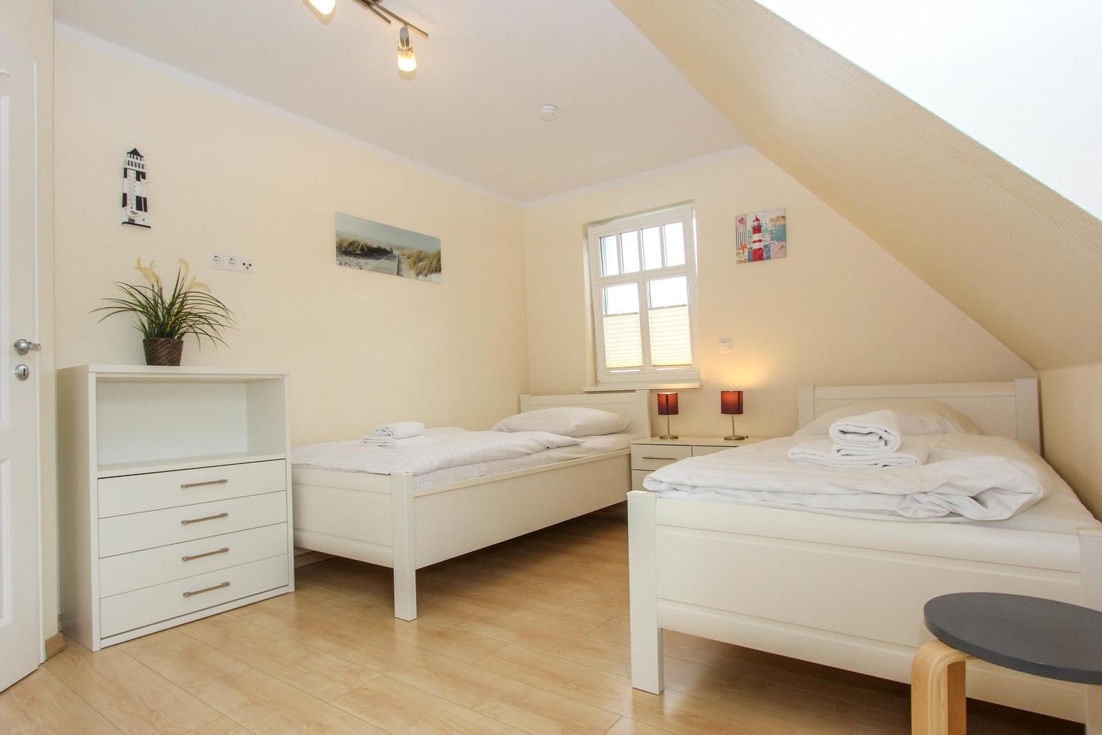 Zimmer mit zwei Betten, Schrank und Fenster unter Dachschräge.