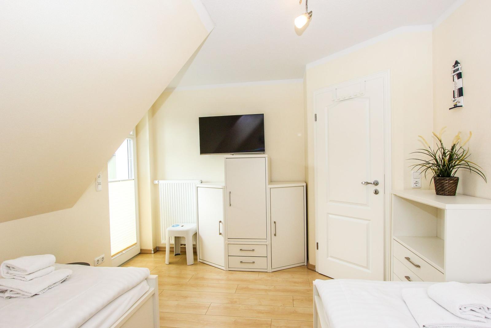 Zimmer mit zwei Betten, TV, Schrank und Pflanze. Dachschräge und Fenster.