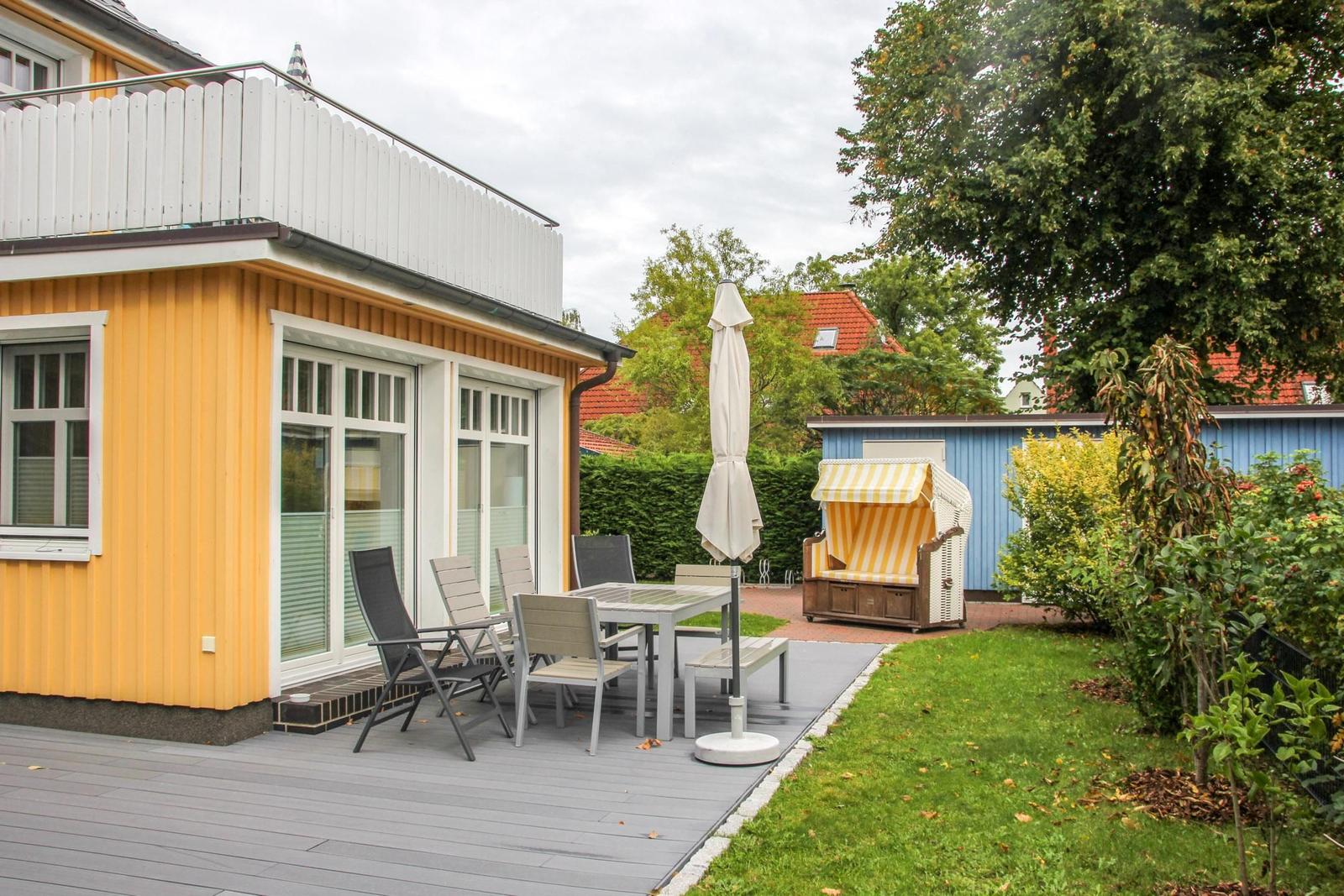 Terrasse mit Tisch, Stühlen und Sonnenschirm neben gelbem Haus mit Garten.