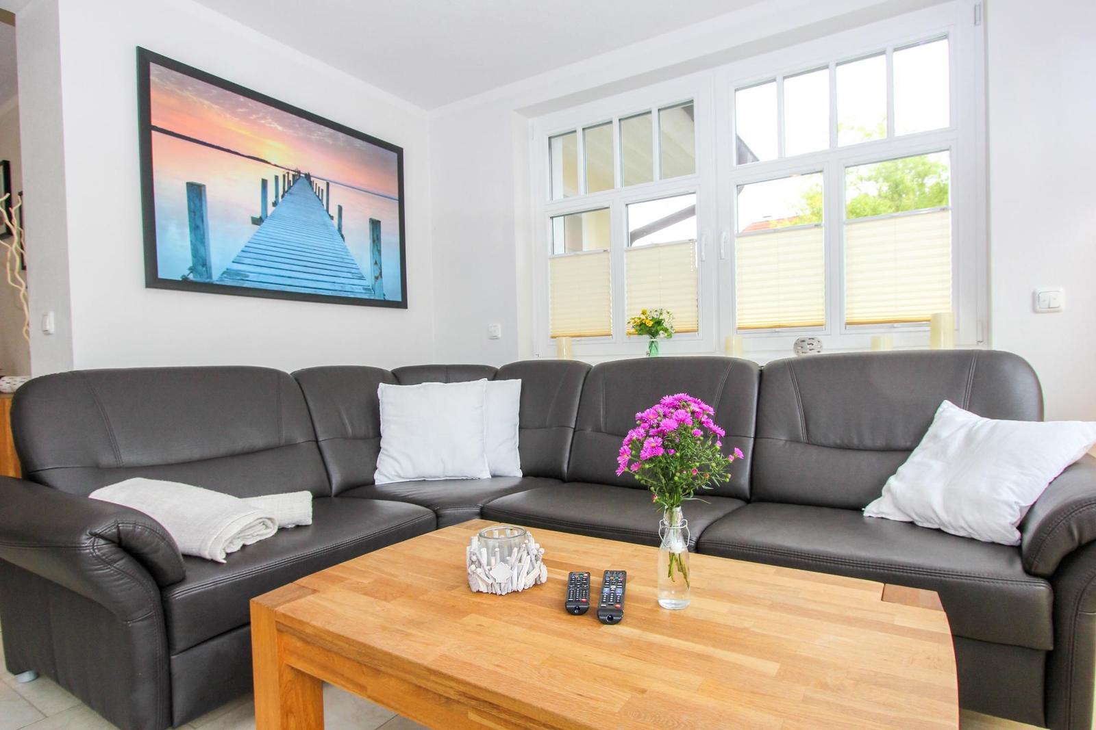 Ein Wohnzimmer mit einem dunklen Sofa, einem Holztisch und großen Fenstern.