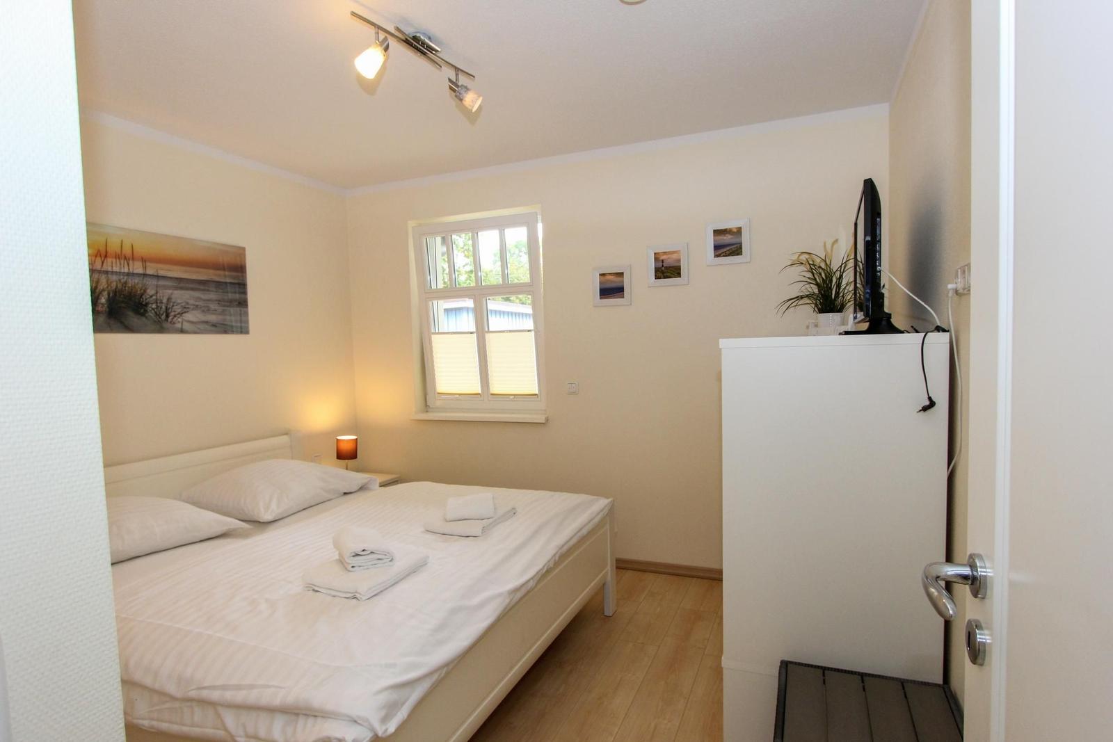 Schlafzimmer mit Bett, Fenster, TV und Wandbildern.