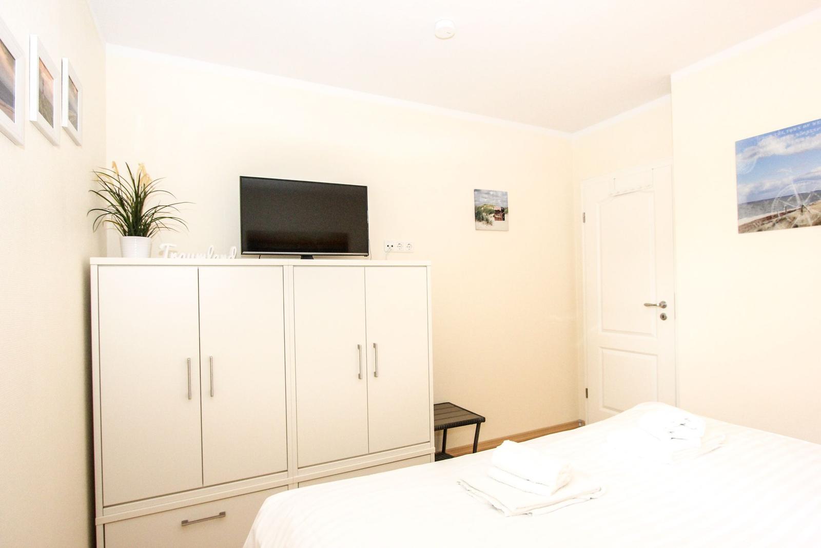 Schlafzimmer mit weißem Schrank, Fernseher und Bett mit Handtüchern.