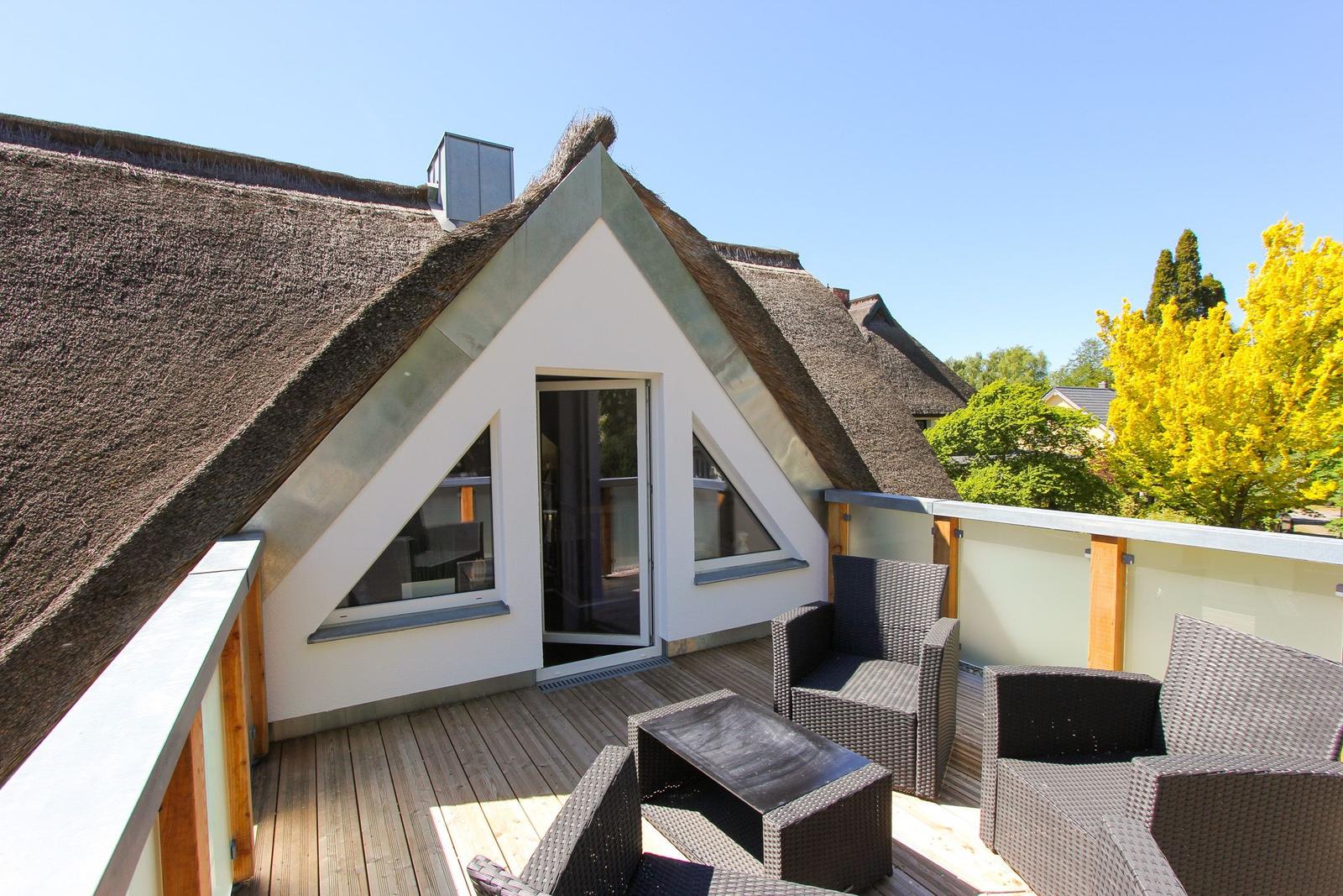 Terrasse mit Sitzgruppe vor einem Haus mit Strohdach und Glasfront.