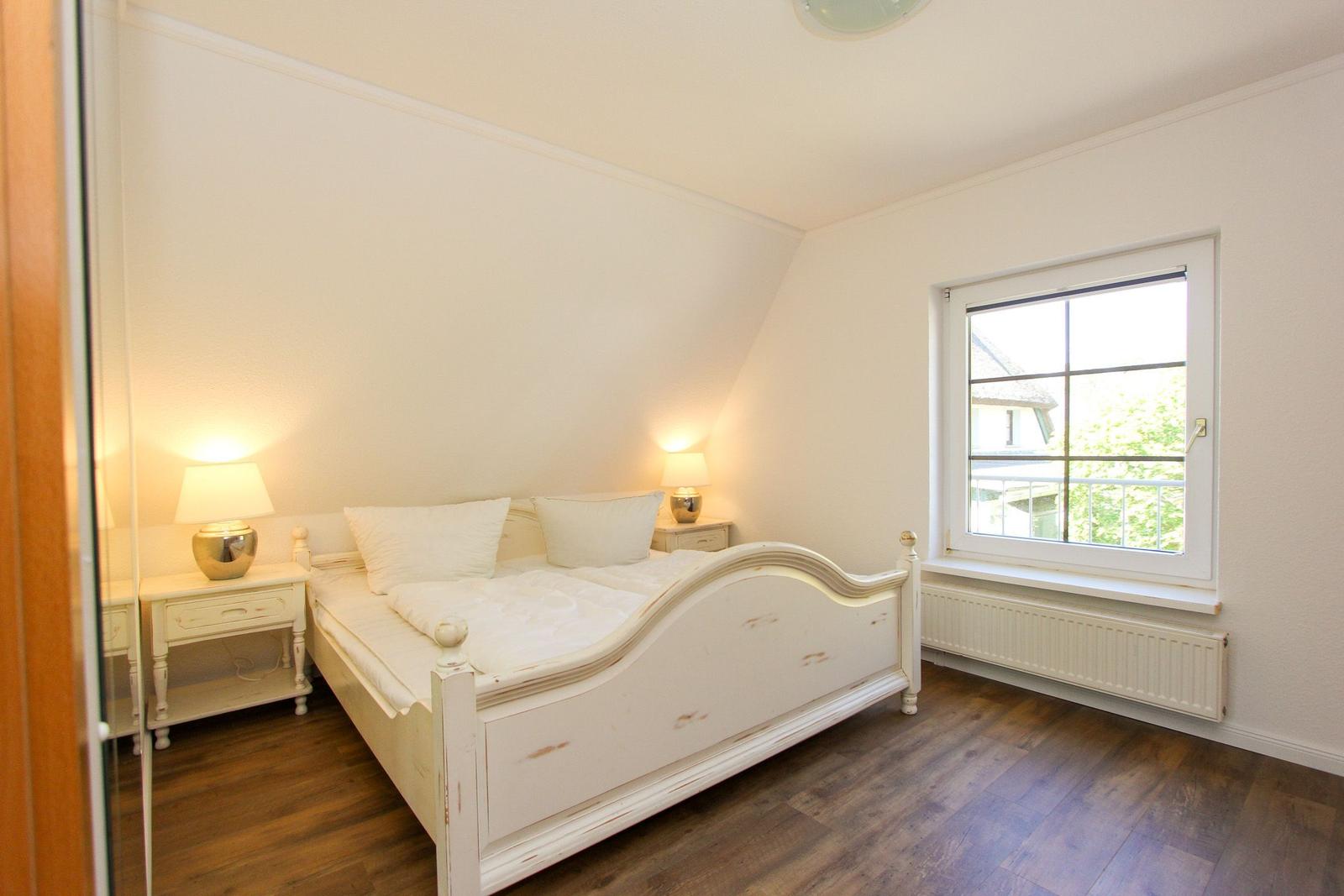 Schlafzimmer mit Doppelbett, zwei Nachttischen und Fenster mit Blick auf Balkon.