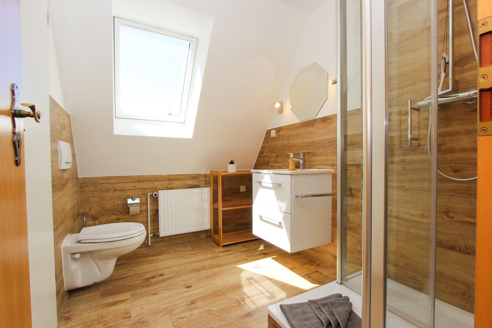 Badezimmer mit Dusche, Waschbecken und Toilette. Holzoptik und Dachfenster.