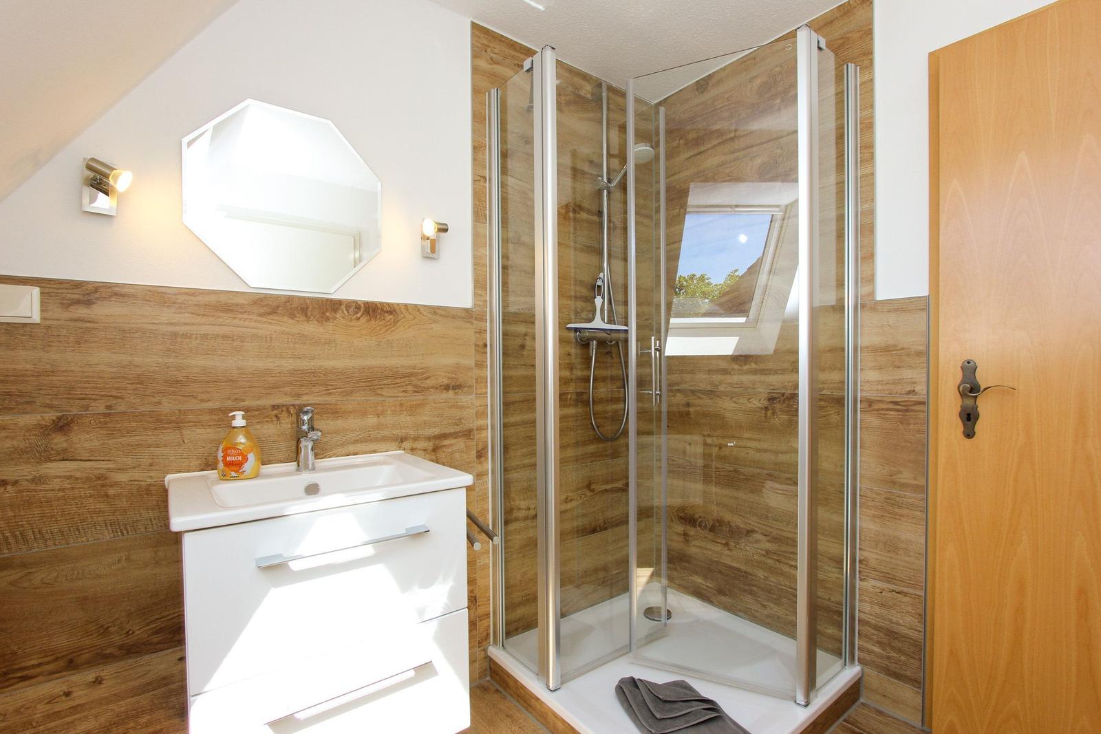 Bad mit Dusche, Waschbecken und Spiegel an Holzwand