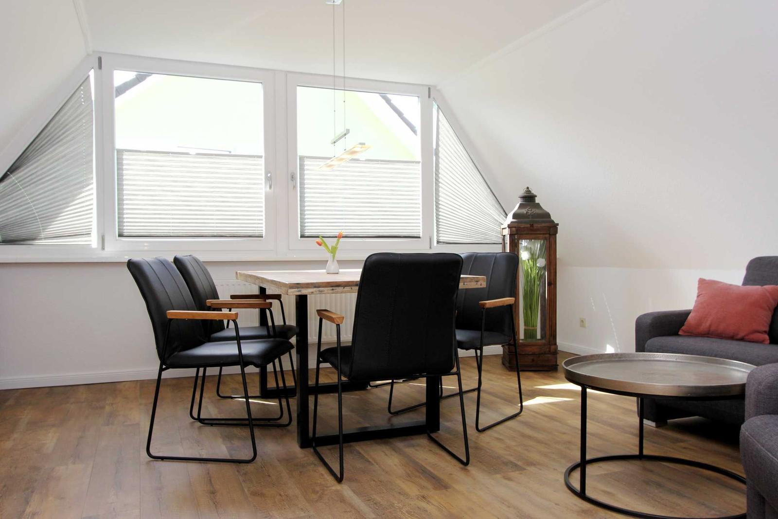 Essbereich mit Tisch, vier Stühlen und großem Fenster. Wohnbereich mit Sofa und Couchtisch.