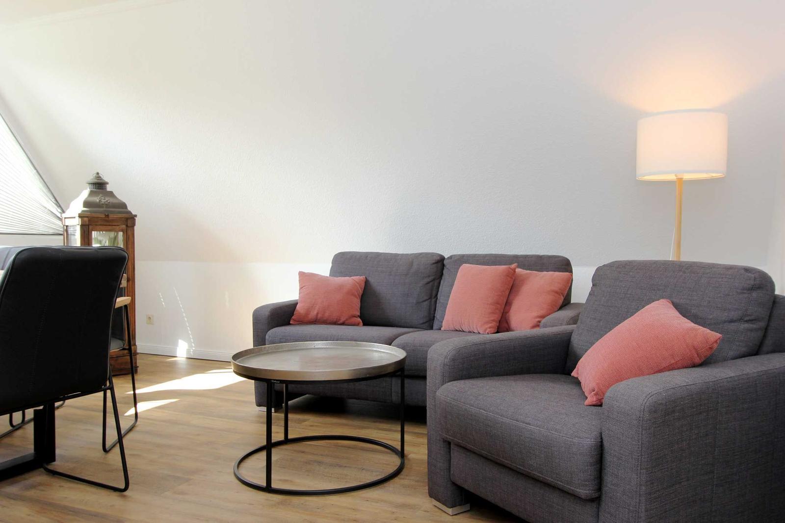 Ein Wohnzimmer mit grauem Sofa, rosa Kissen, Tisch und Stehlampe.
