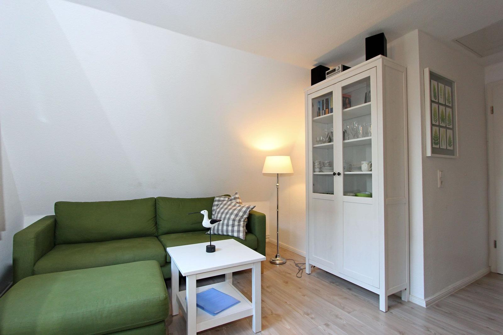 Ein Wohnzimmer mit grünem Sofa, weißem Tisch und Glaswand-Schrank.