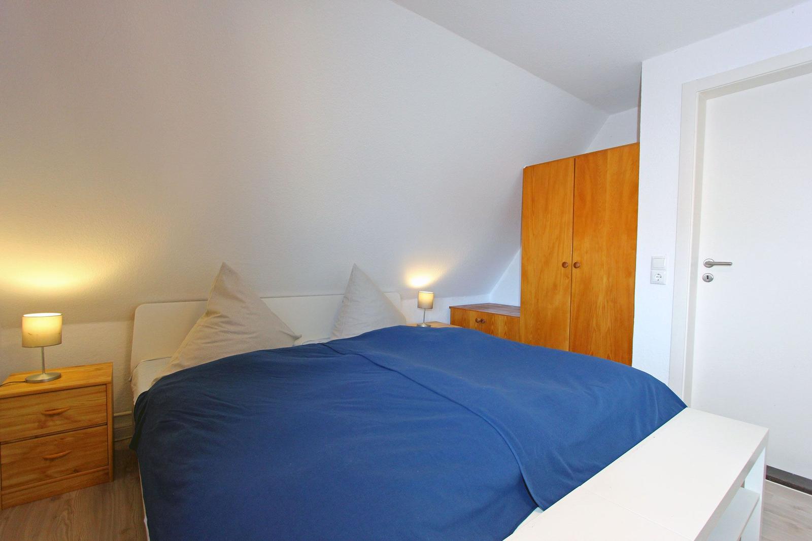 Schlafzimmer mit Bett, Nachttischen und Kleiderschrank unter Dachschrägen.