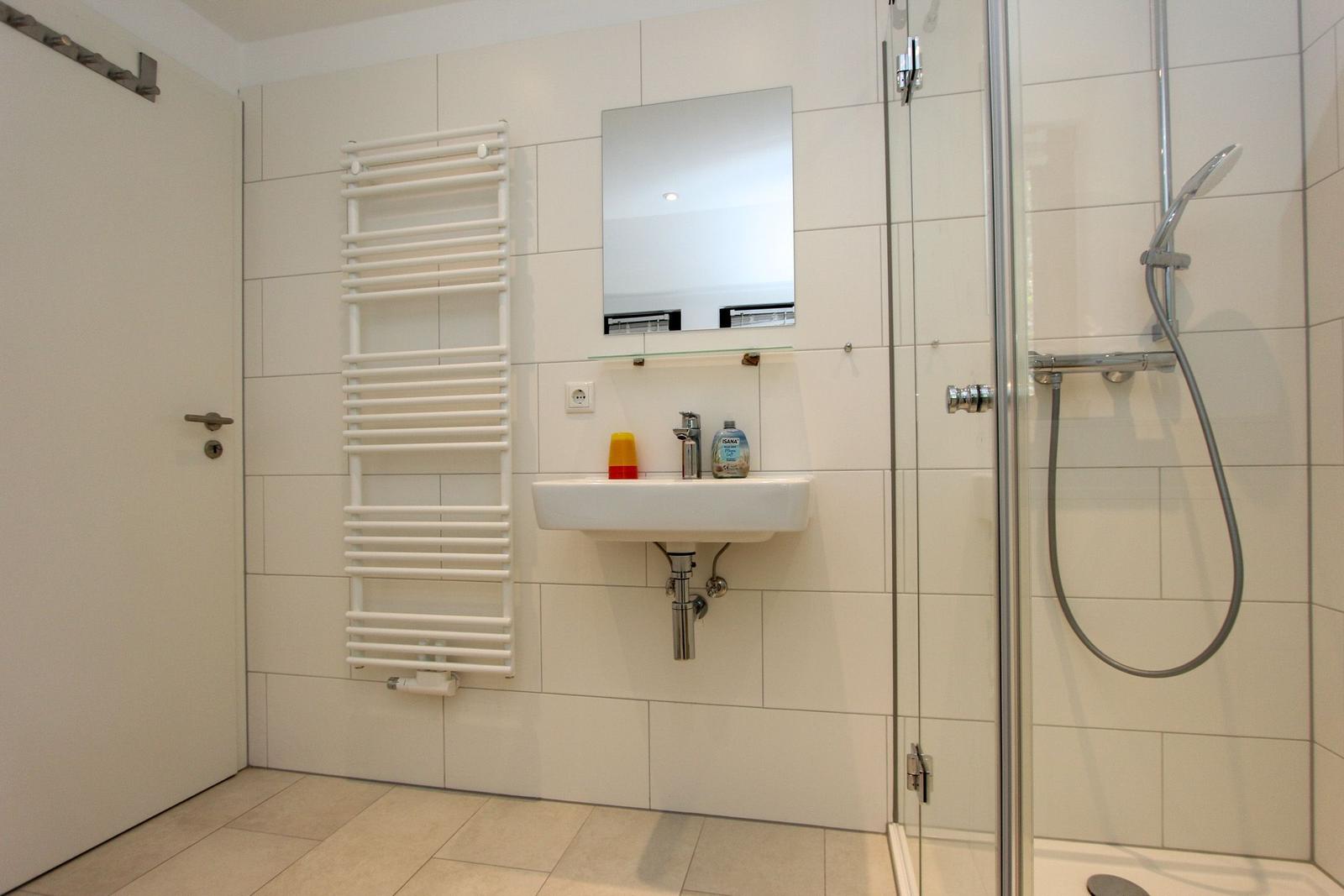 Badezimmer mit Dusche, Waschbecken und Heizkörper