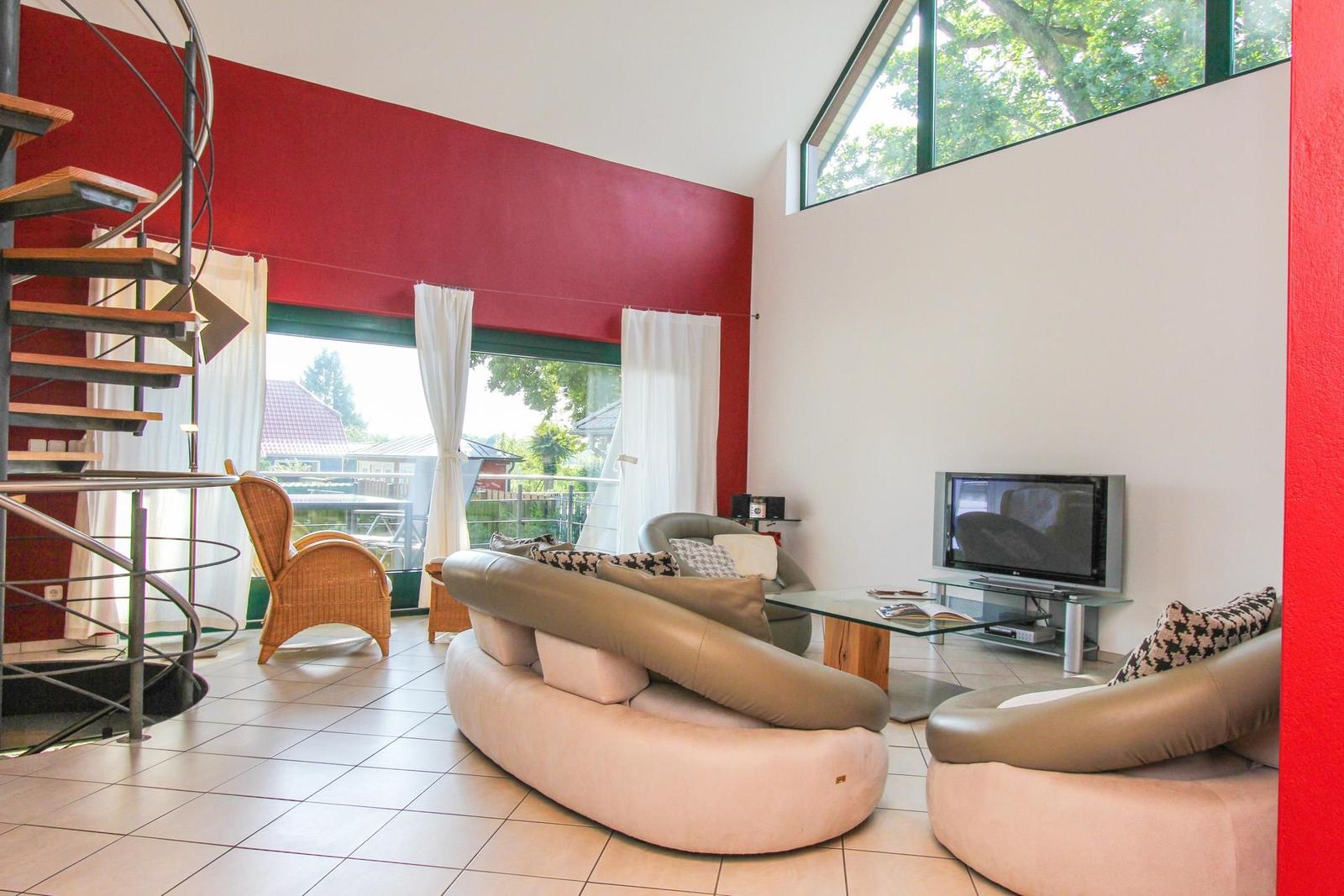 Wohnzimmer mit螺旋楼梯, Sofa, Fernseher und großem Fenster mit Blick auf Garten.